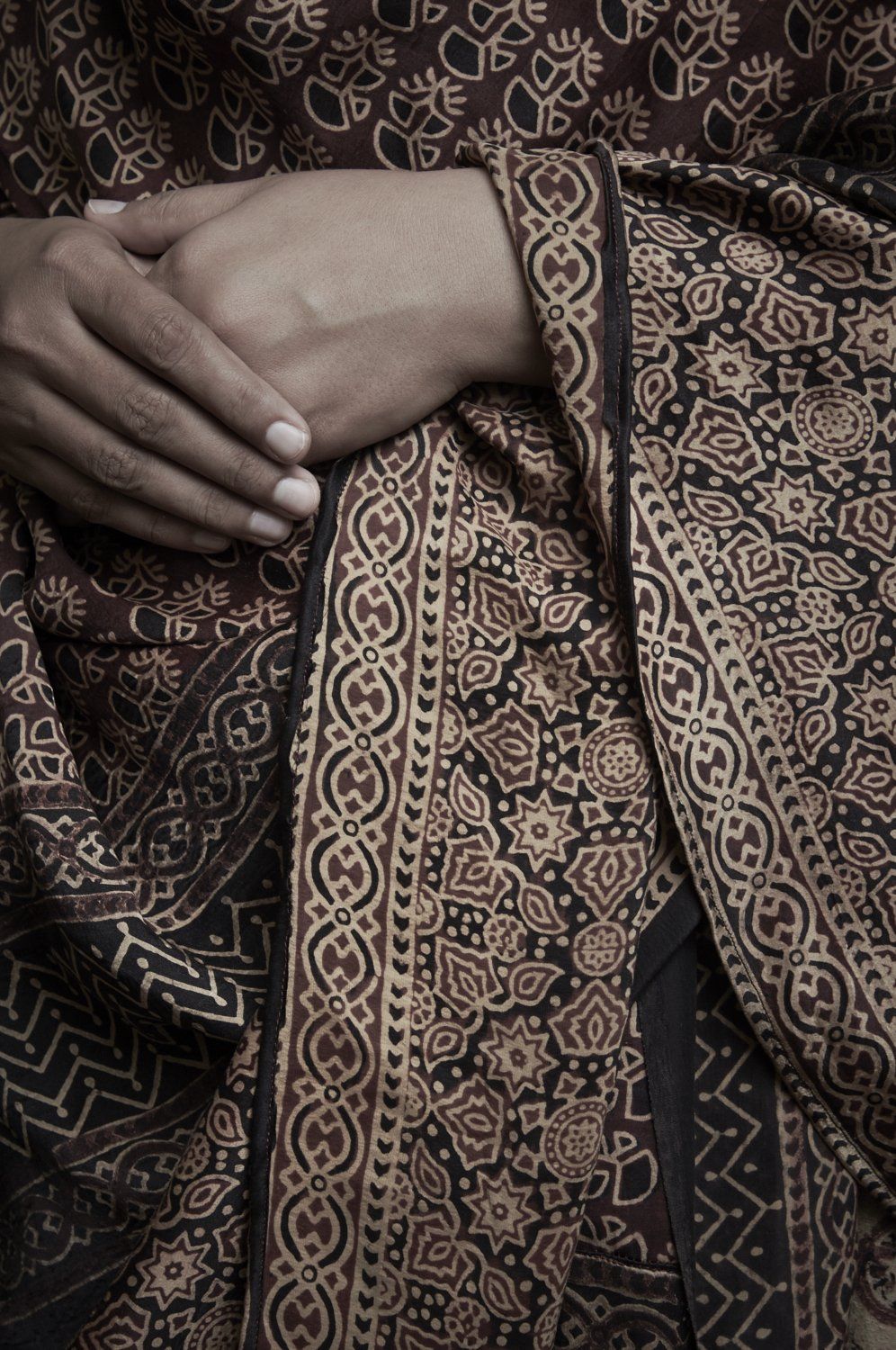 Hands clasped over patterned brown fabric on a person’s lap