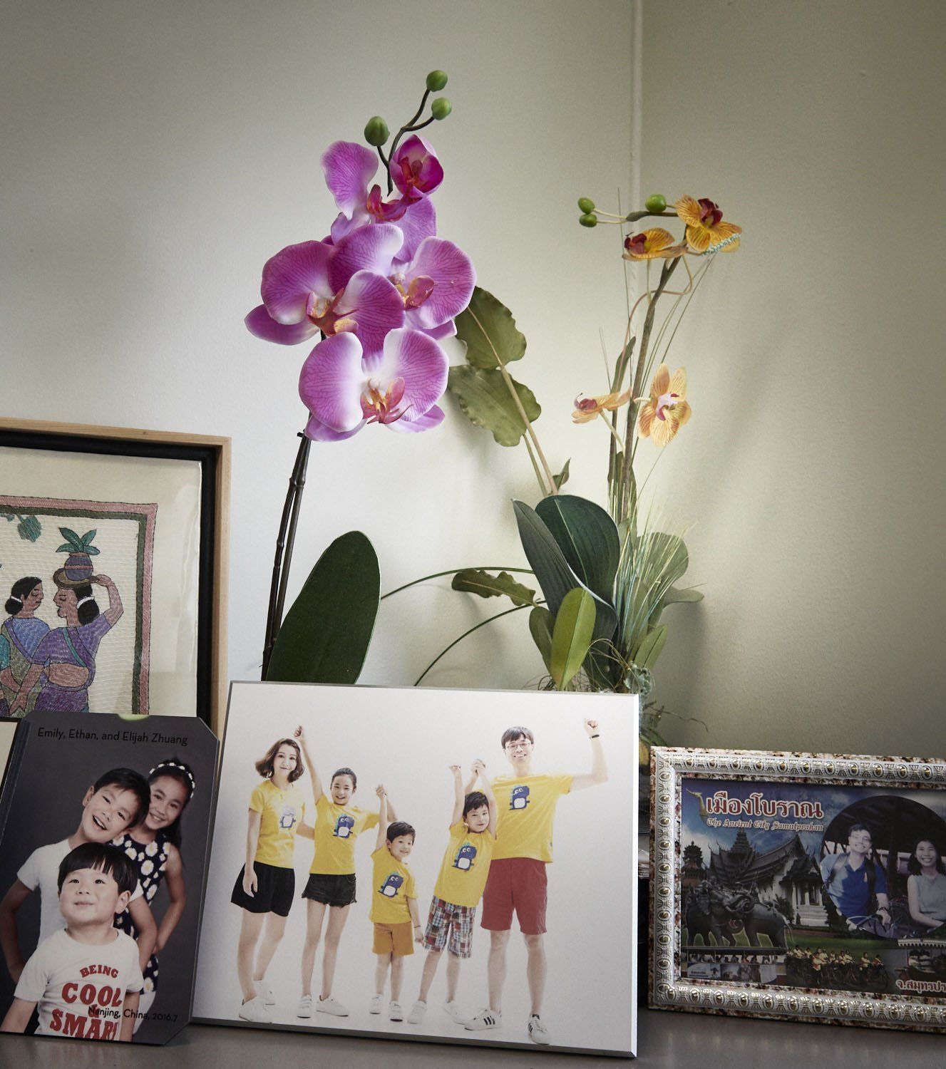 Orchid and other flowers behind framed family and group photos on a shelf