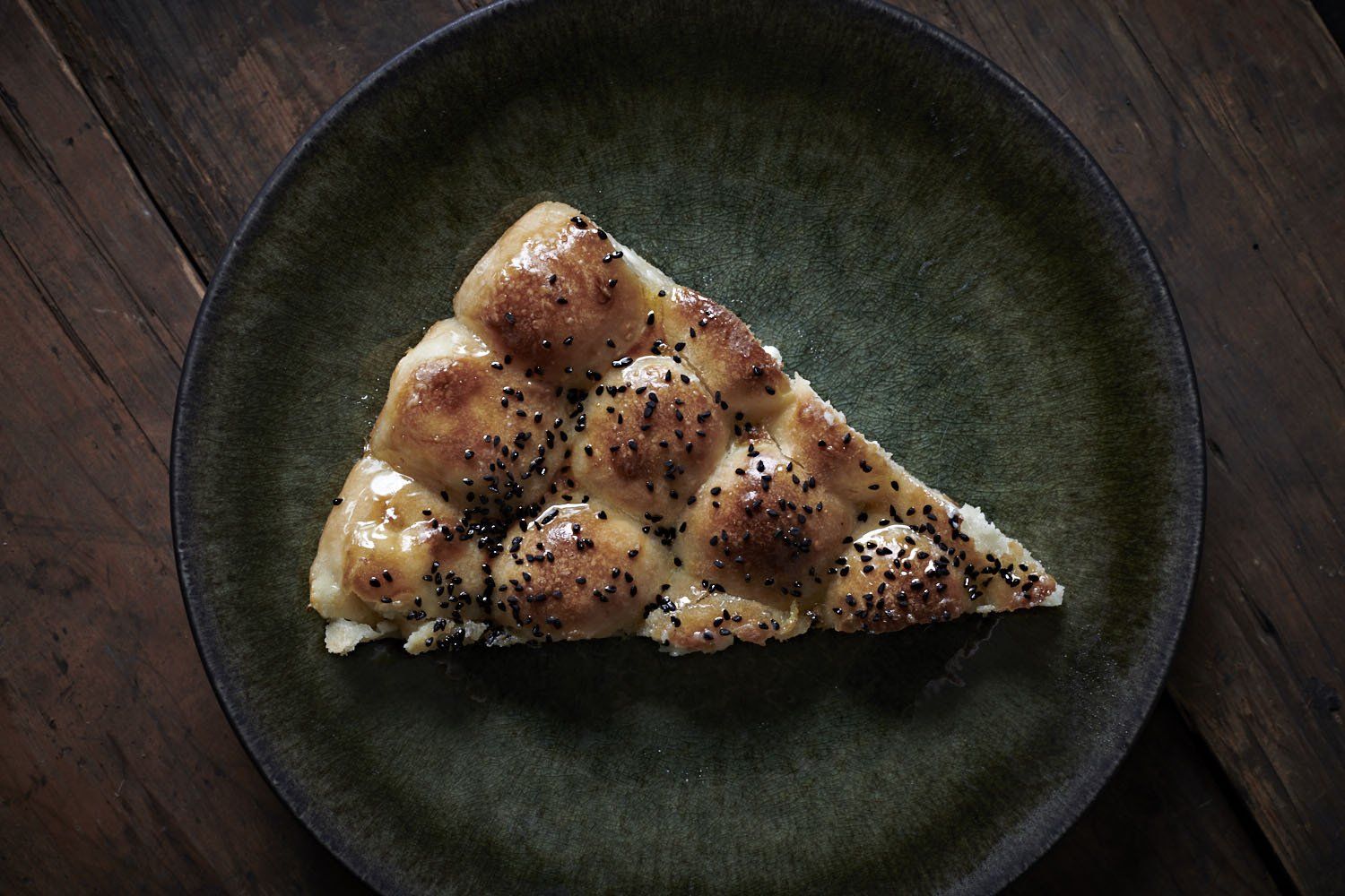 Slice of pepperoni pizza on a dark green plate on a wooden table