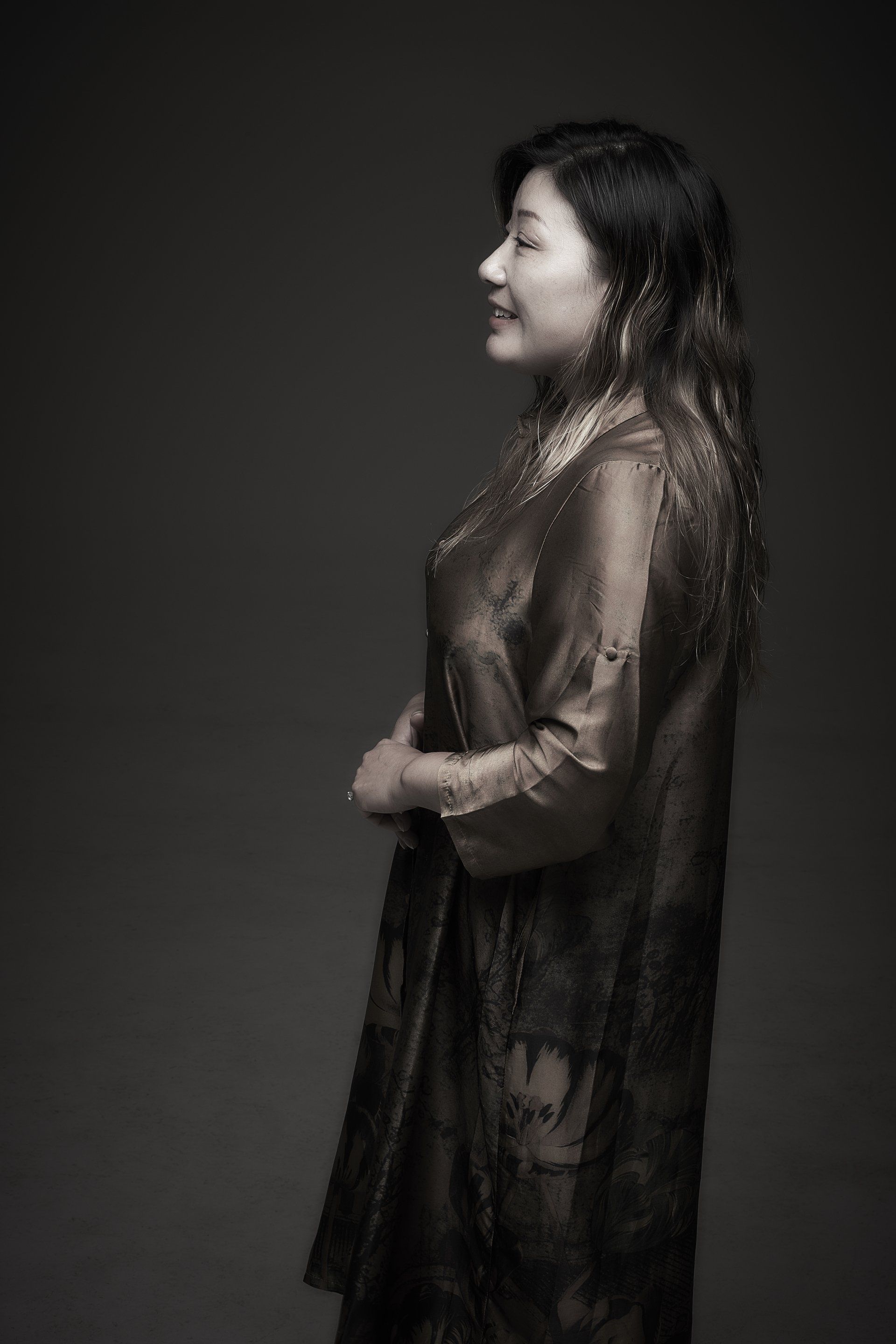 Side-profile portrait of a woman in a dark dress against a black background