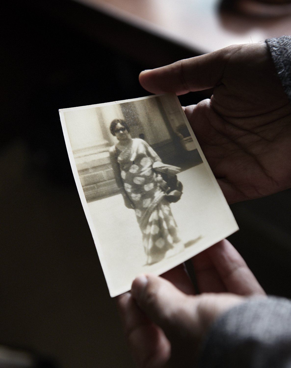 Hands holding a small old black-and-white photo of a person in a patterned garment