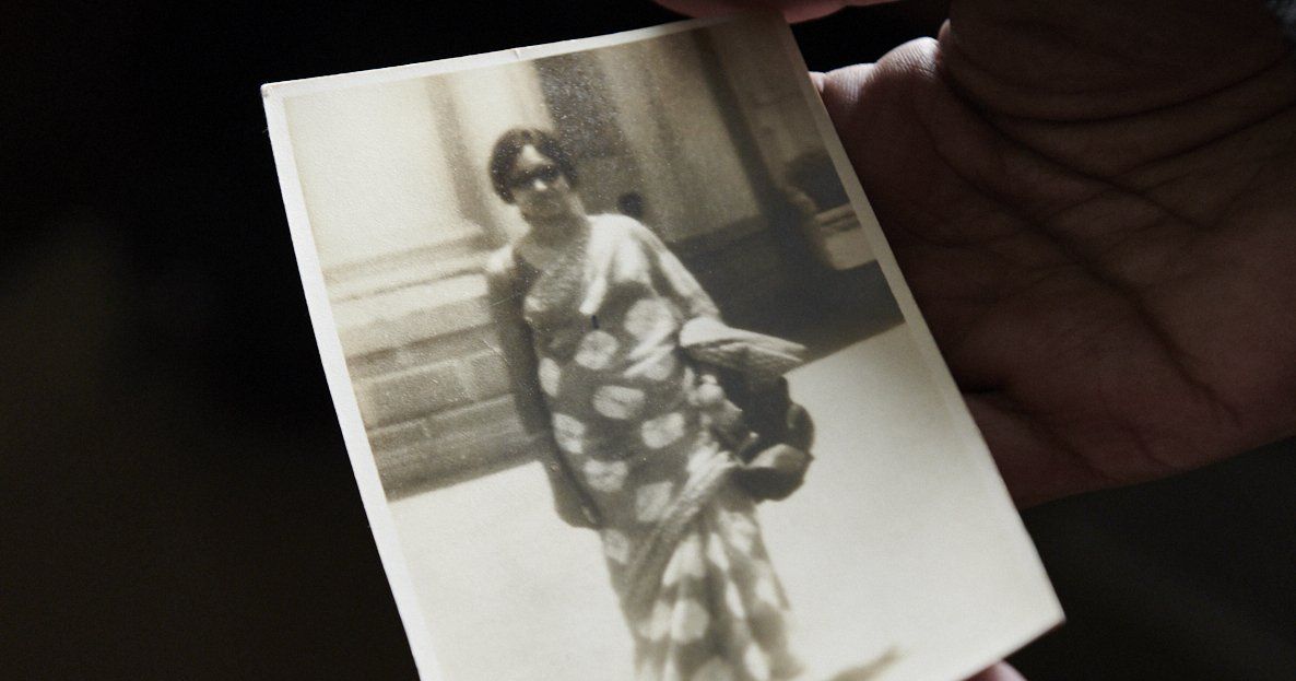 Small black-and-white photo of a person in patterned clothing being held in a hand outdoors.