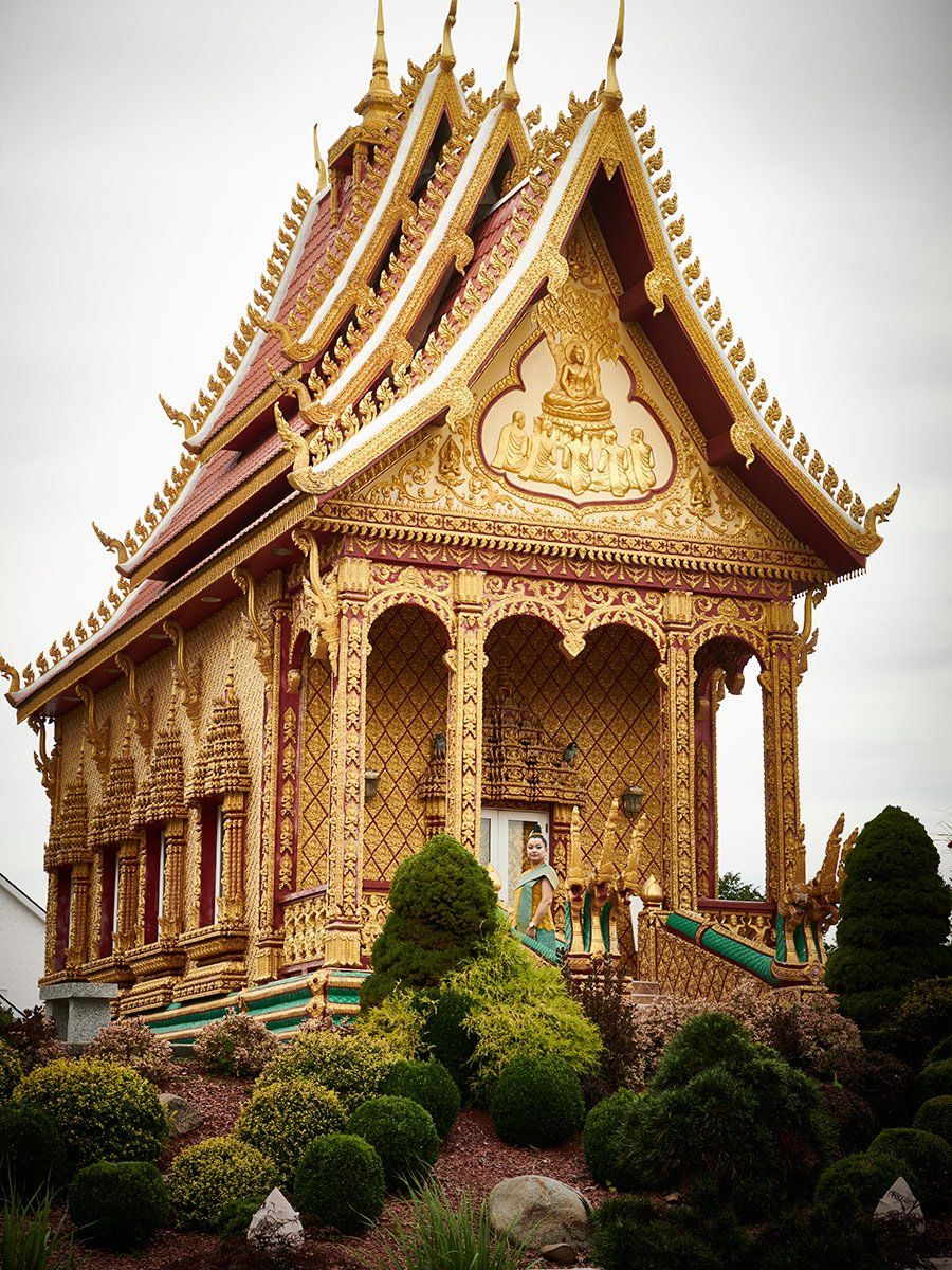 Ornate golden Thai temple with a red roof, framed by lush green shrubs and trees