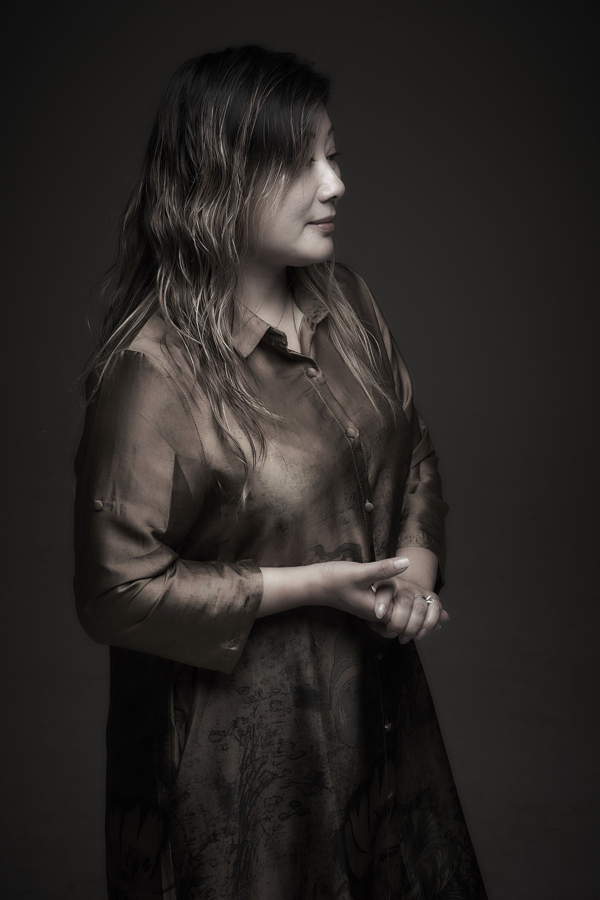 Portrait of a person in a dark dress, standing in profile against a dim background, with a textured overlay.