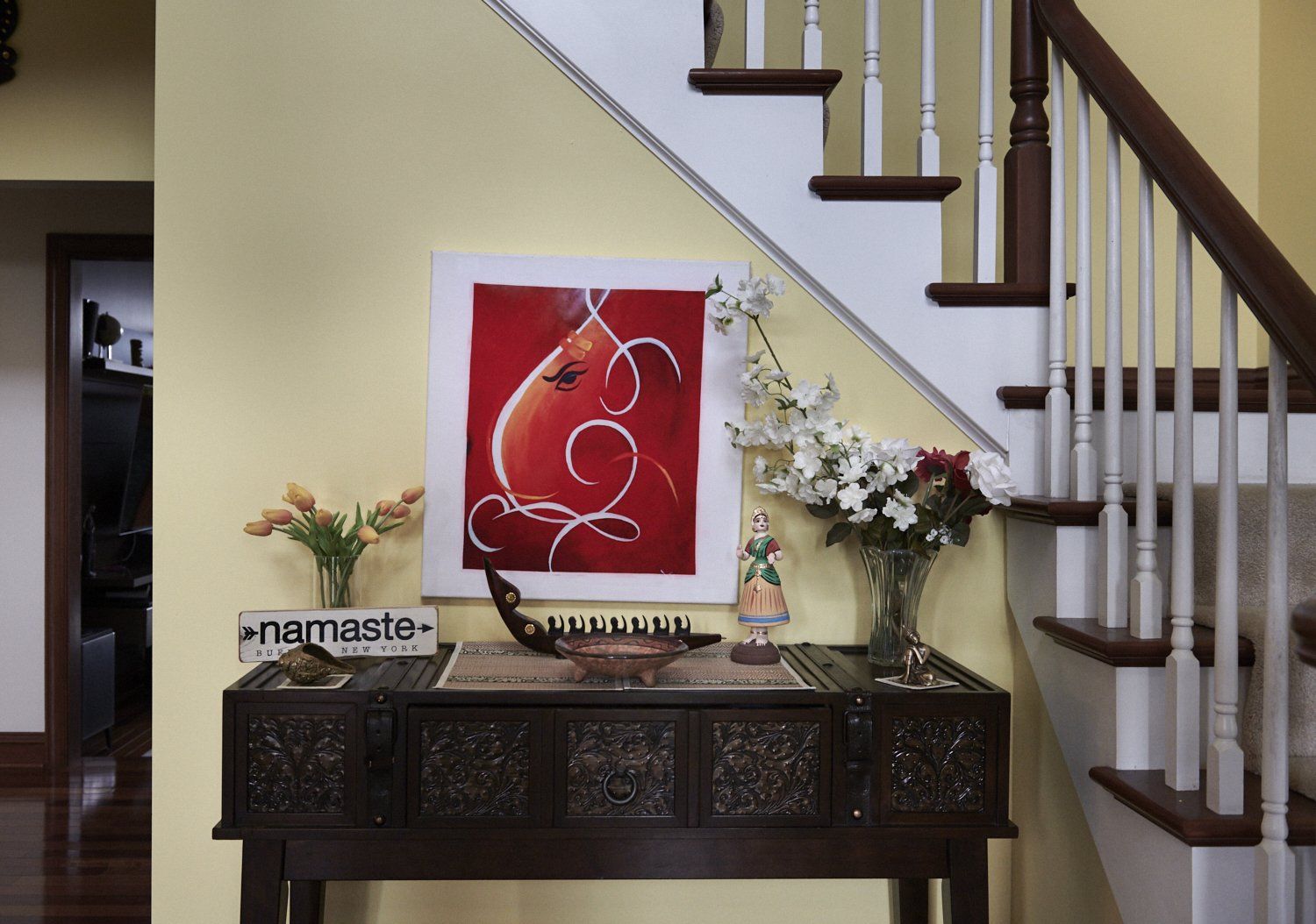 Entryway console table under staircase with red art, flowers, and decorative items