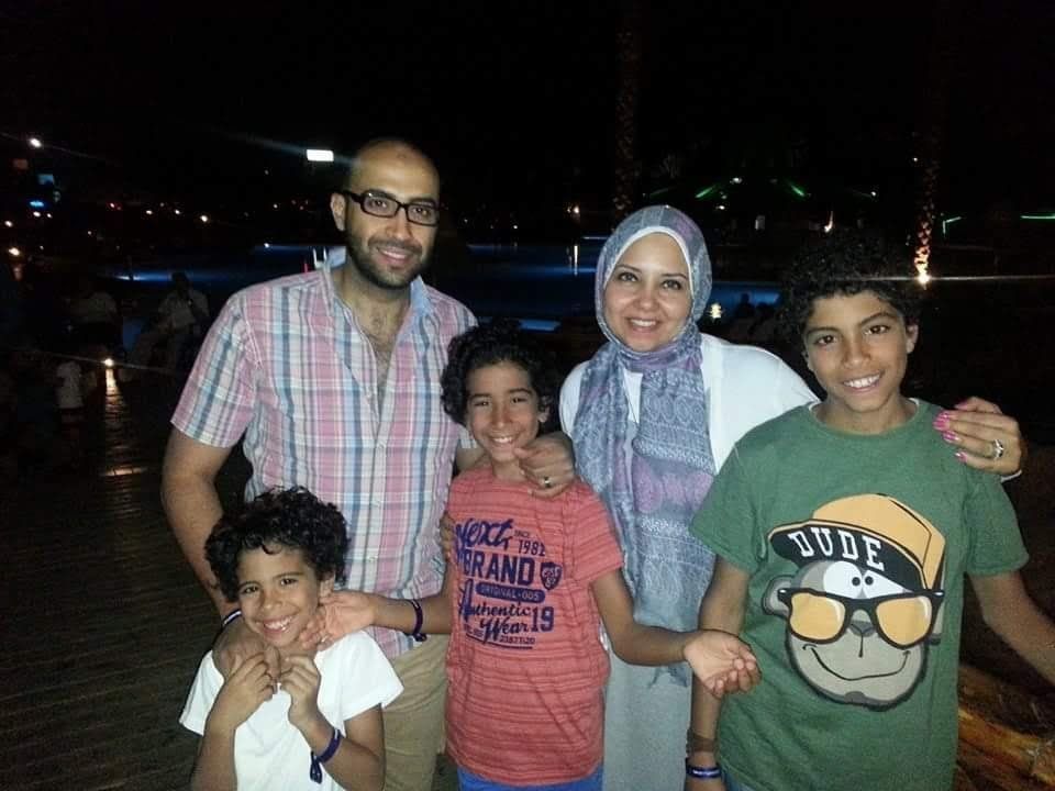A family of five smiling outdoors at night, standing close together in front of lights.