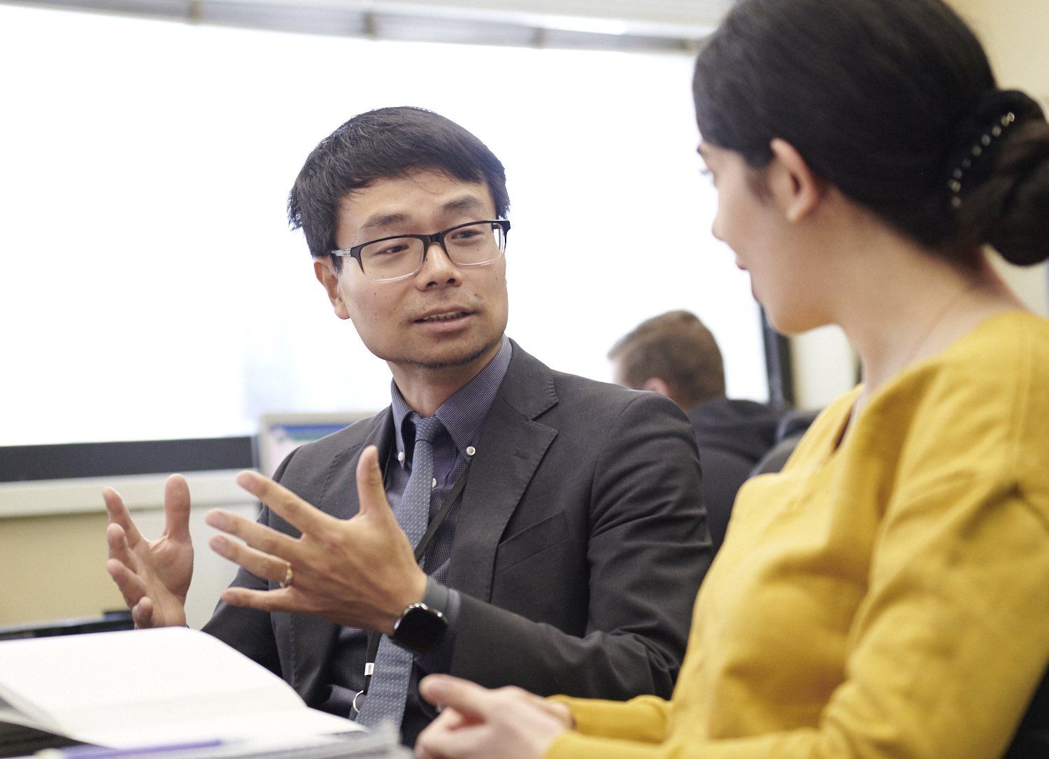 Two people in a meeting, talking across a table in an office setting.