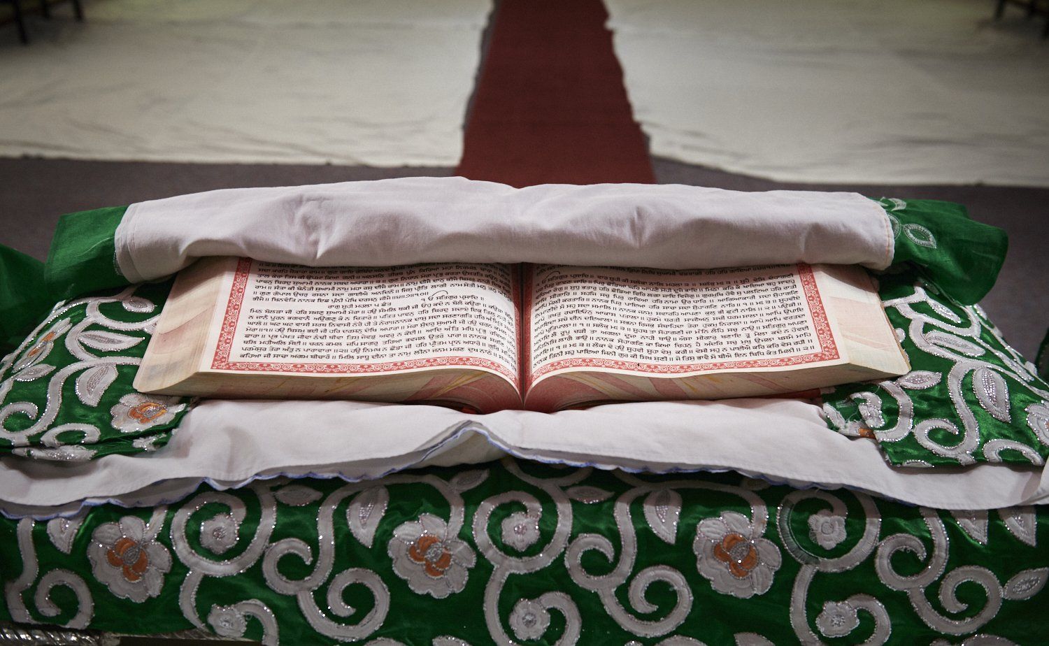 Open book on a green patterned cloth, with a rolled white cushion behind it.