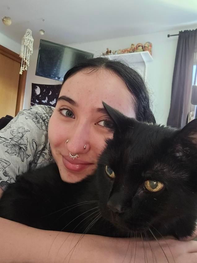 Woman lying beside a black cat in a cozy bedroom, both looking at the camera.