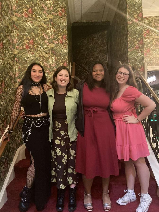 Four women posing together indoors, smiling in colorful dresses and boots.