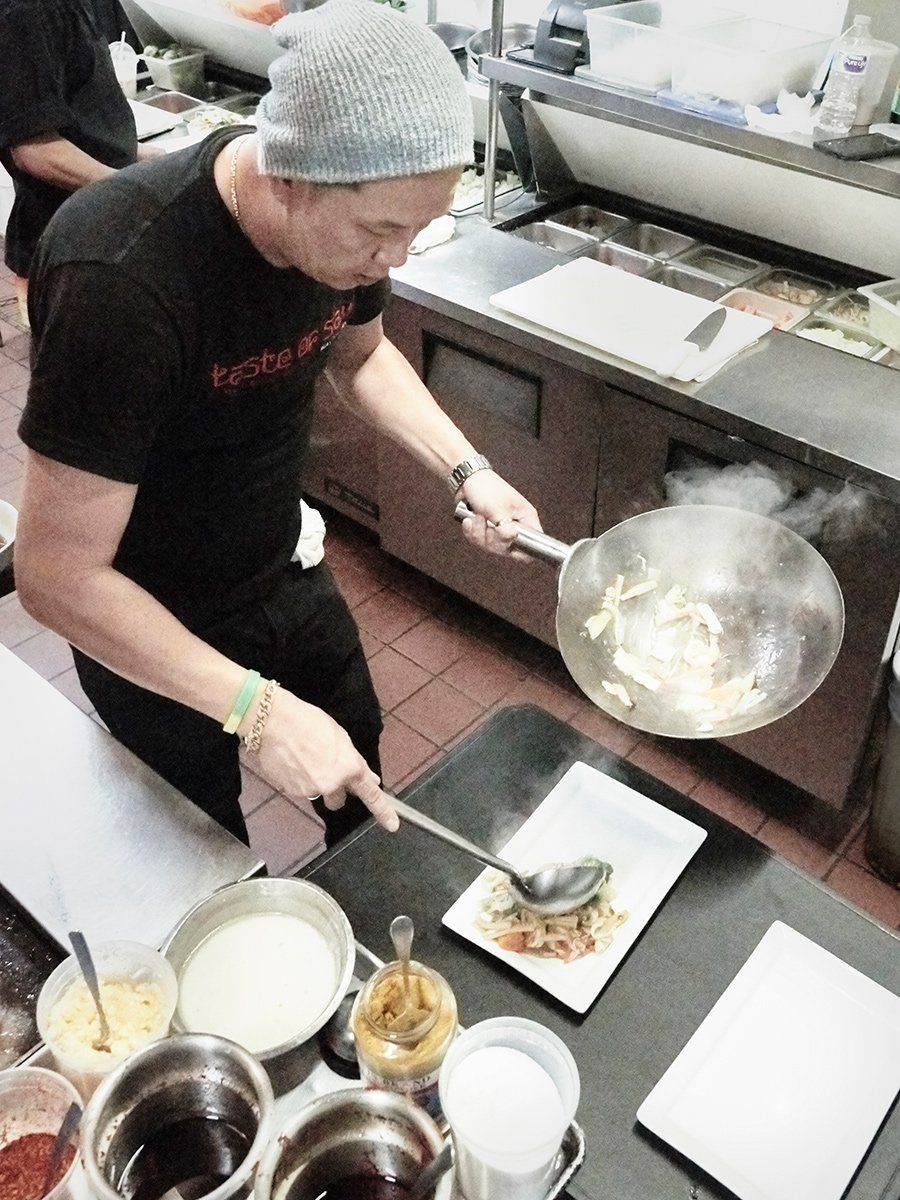 Chef plating food beside a steaming wok in a restaurant kitchen