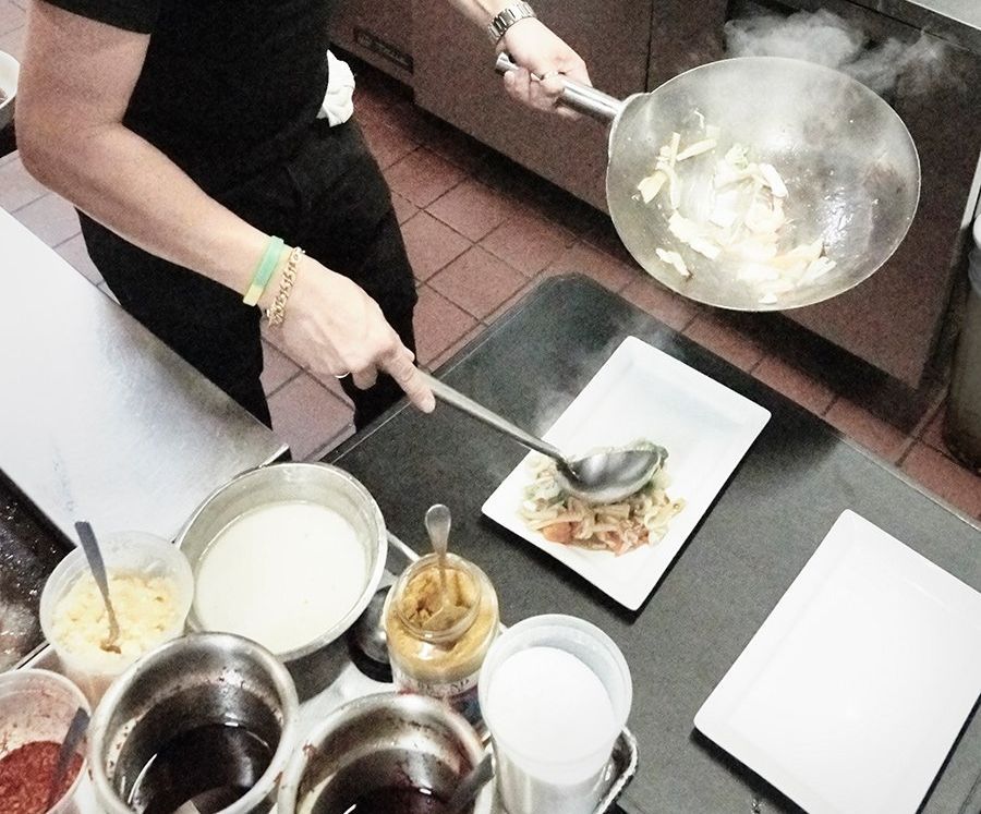 Person plating food from a wok onto a white plate on a kitchen counter