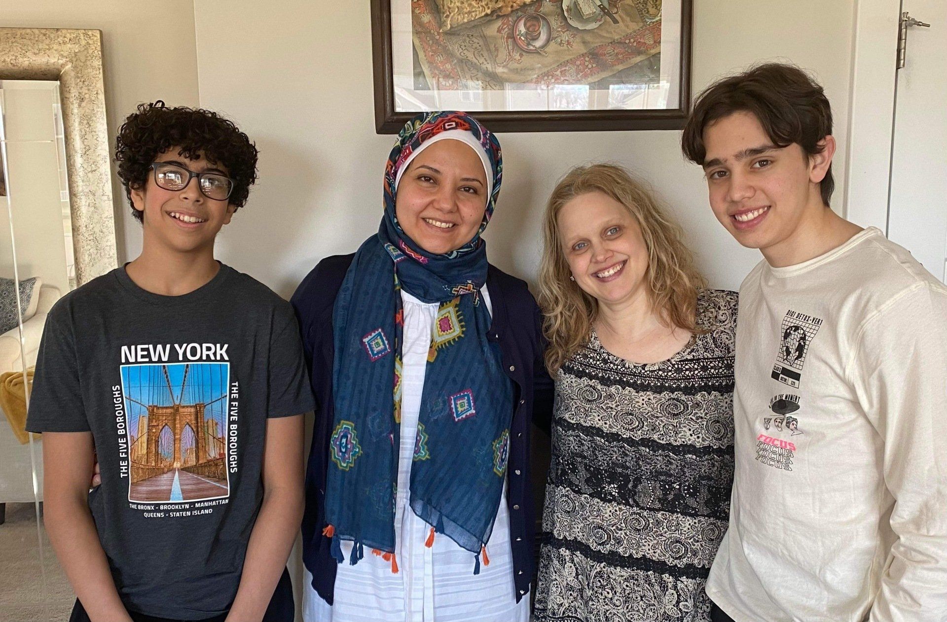 Four people smiling indoors, standing in front of a framed wall hanging.