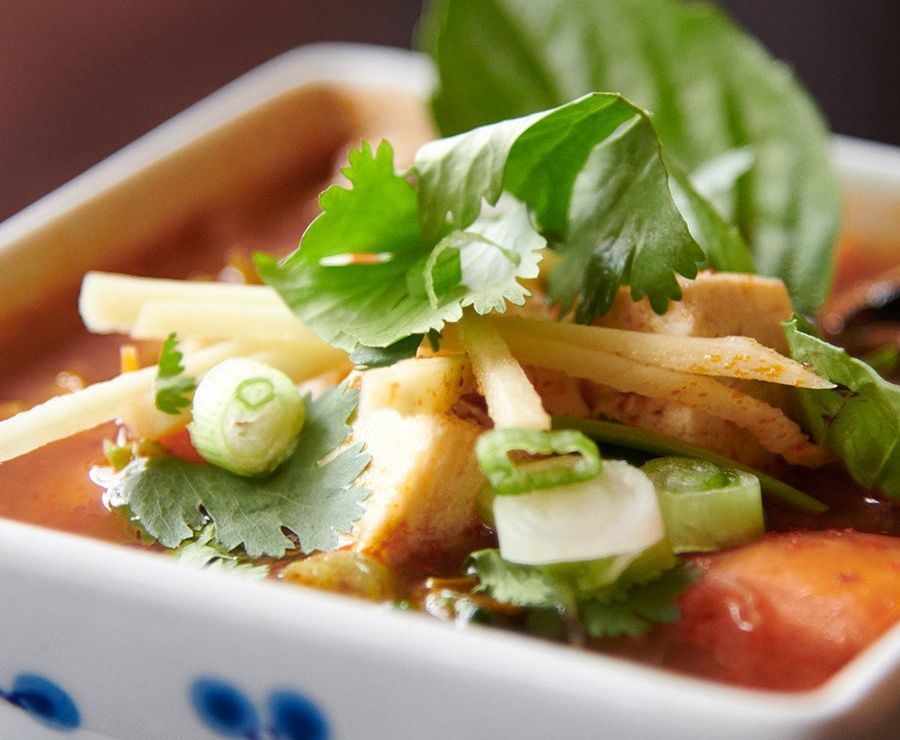 Close-up of a Thai curry bowl topped with basil, cilantro, and sliced green onions