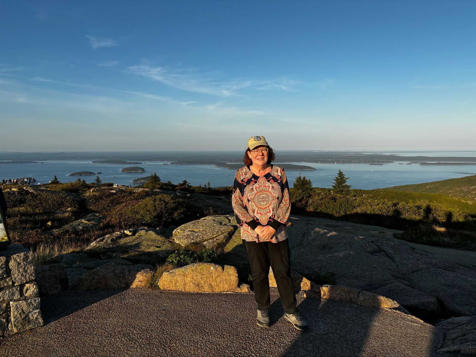 Person standing on rocky overlook with ocean and islands in the background at sunset