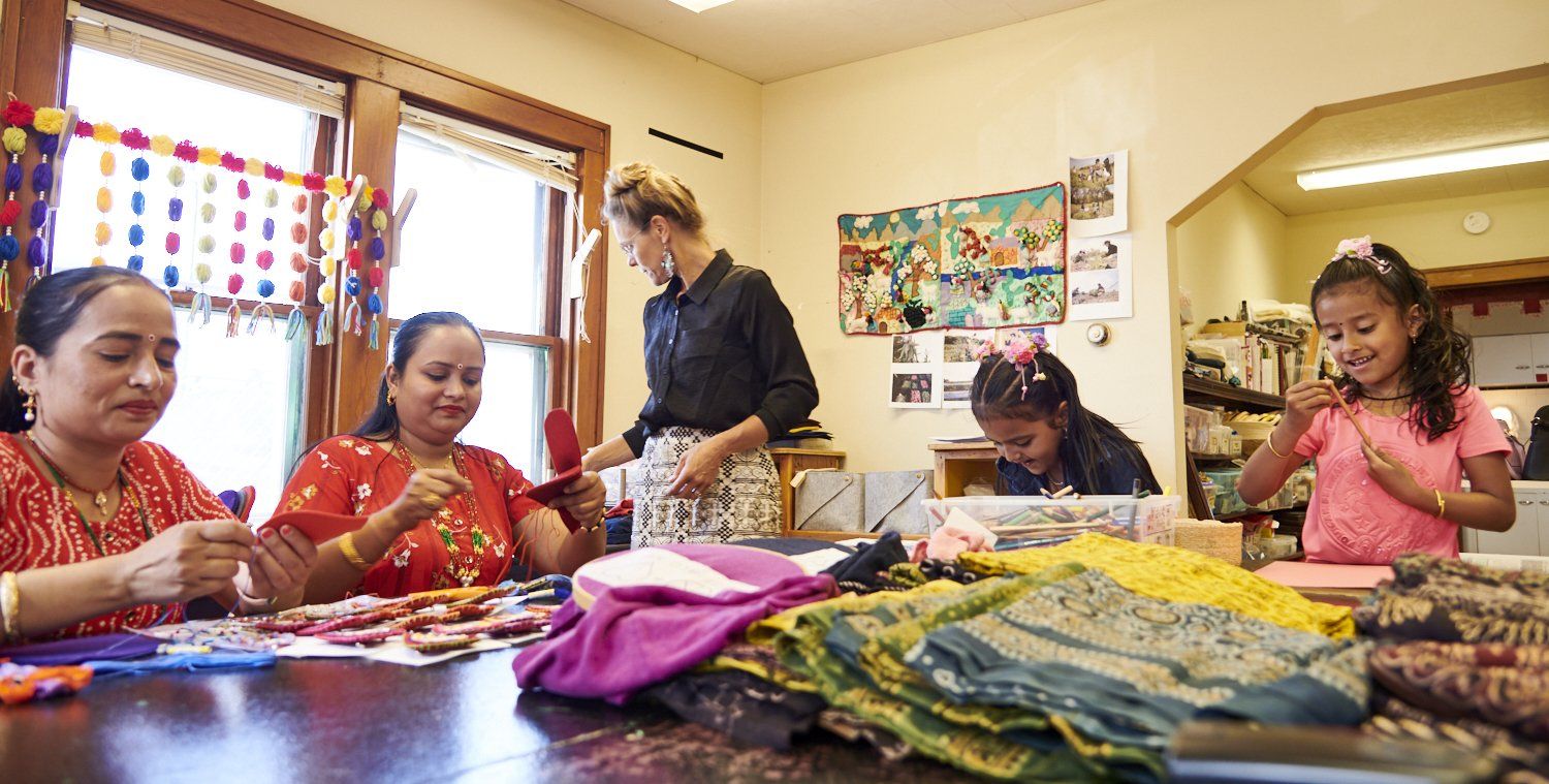 People working at a table with colorful fabric and crafts in a bright room