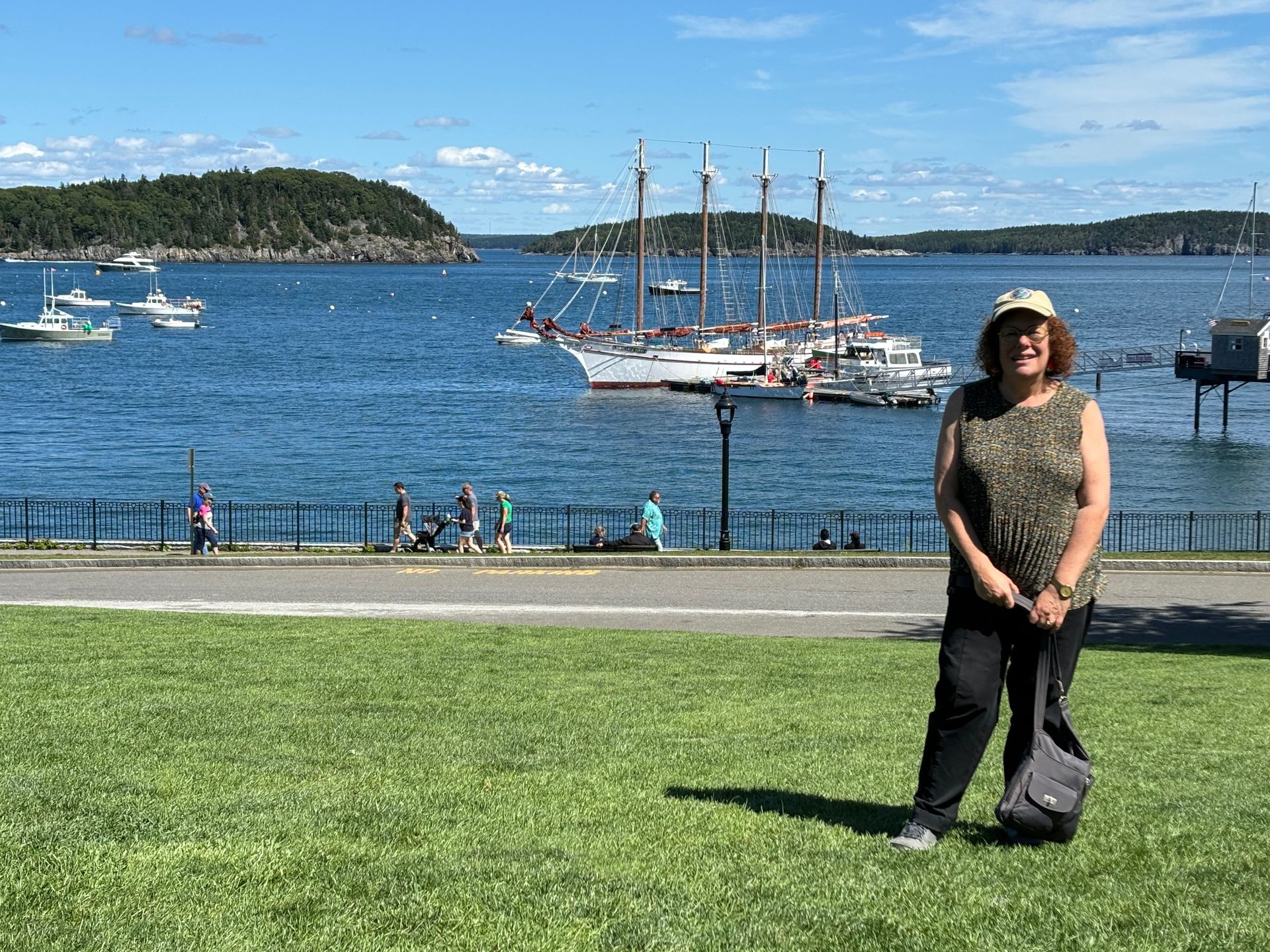 Woman standing on a grassy waterfront with sailboats and a blue bay in the background