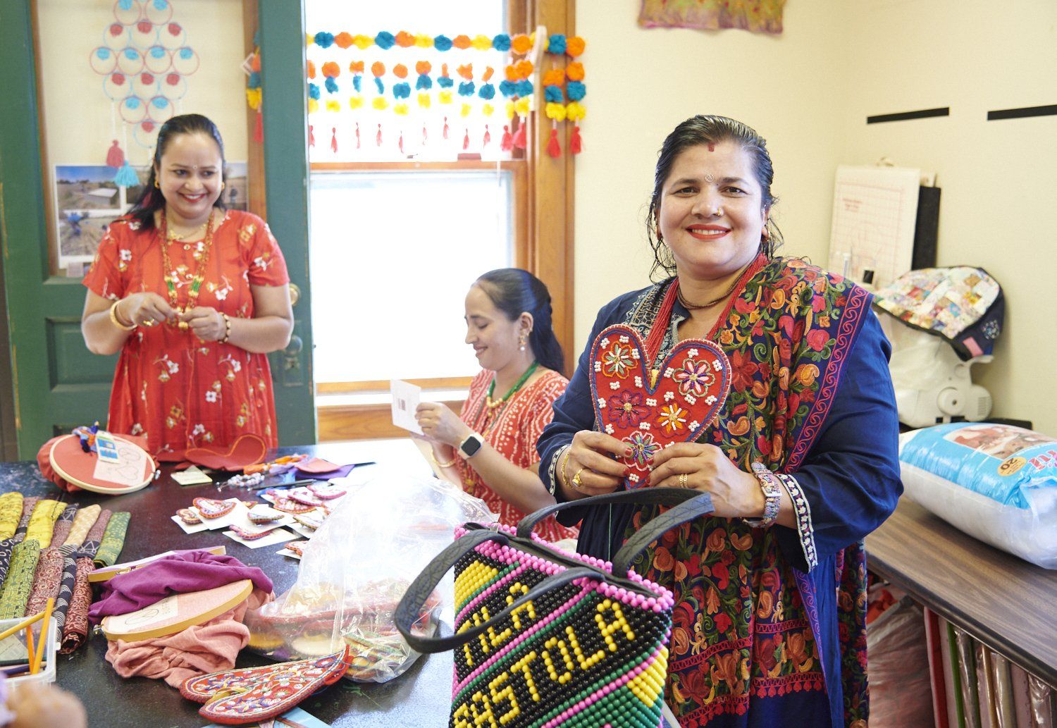 Two women smiling at a craft table with colorful handmade items in a bright room