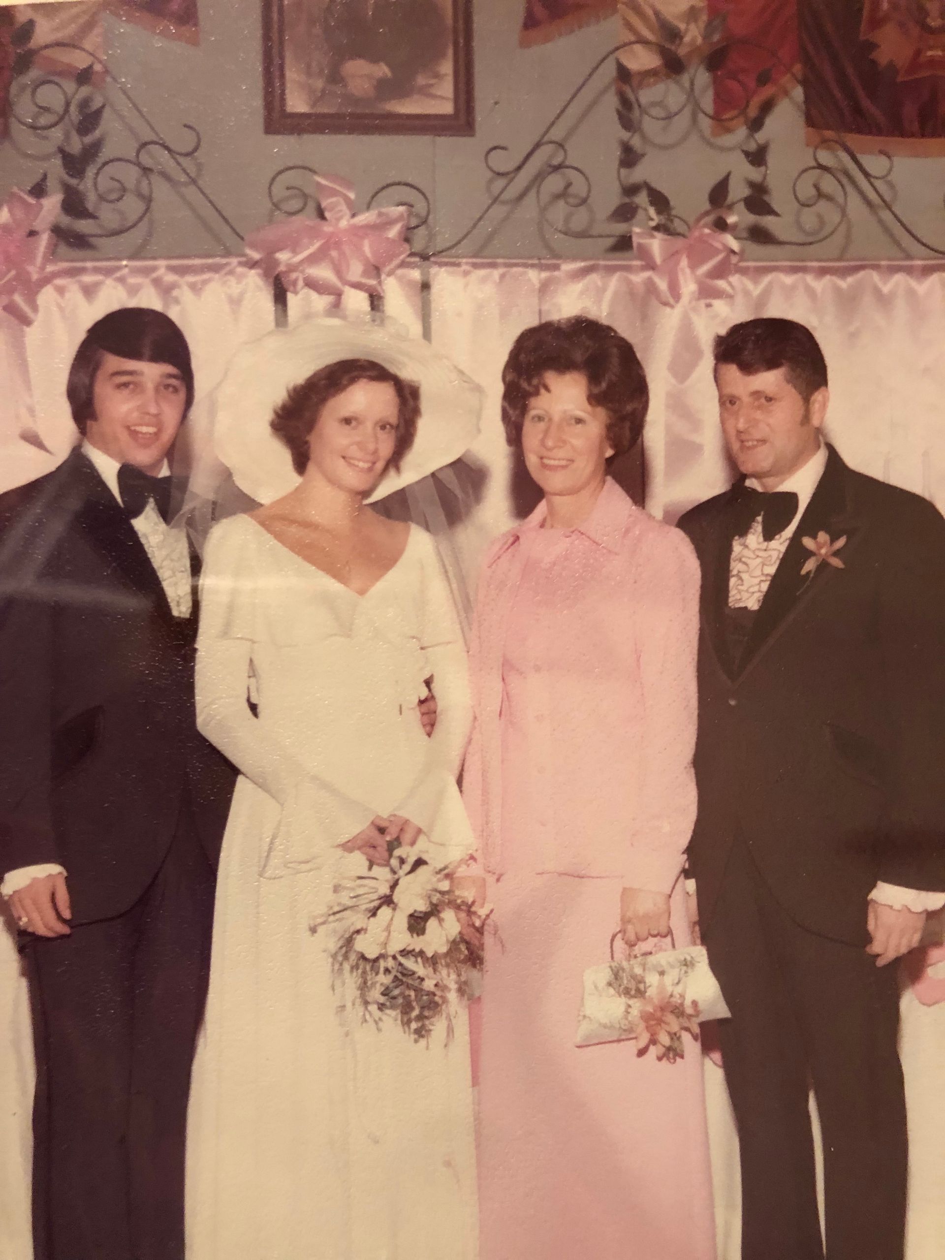 Four people in formal attire posing at a wedding, with two women holding bouquets.