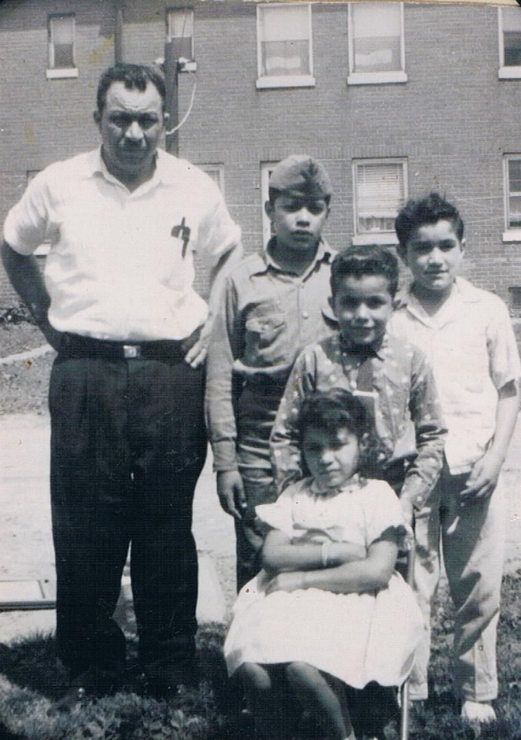 Black-and-white group portrait of four children and one adult standing outdoors in front of a building