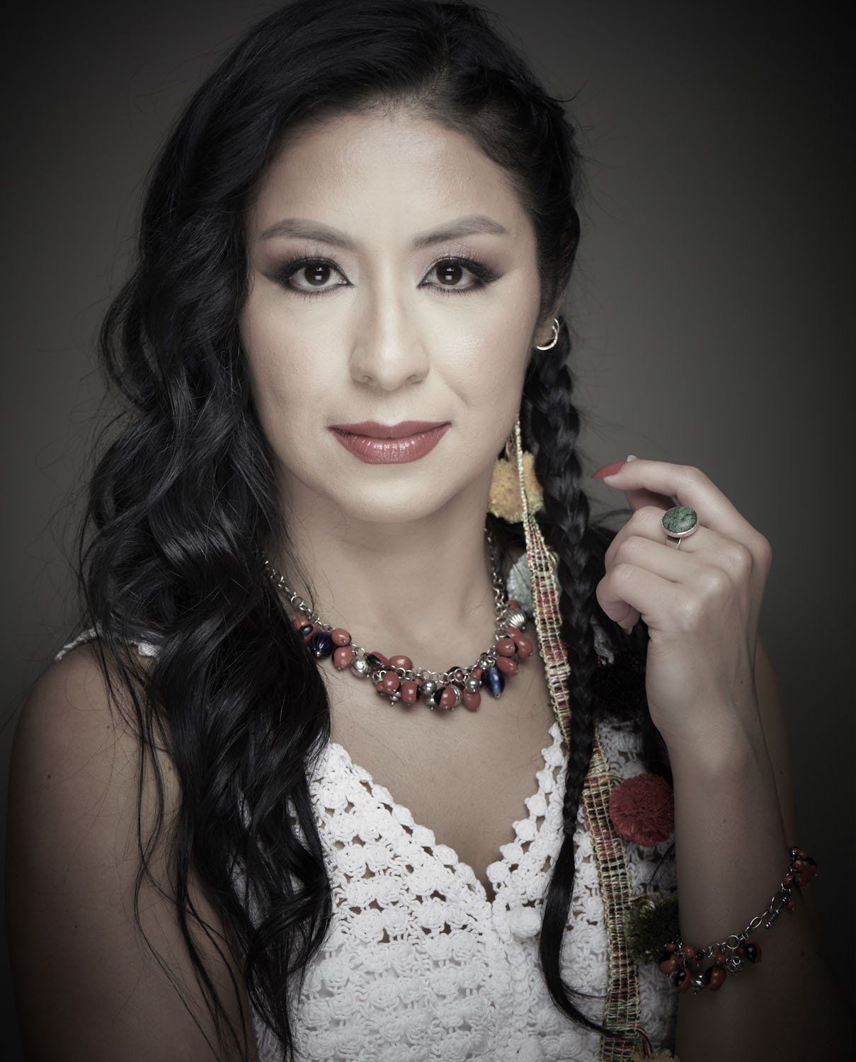 Portrait of a woman in a white dress with long dark hair and jewelry against a dark background