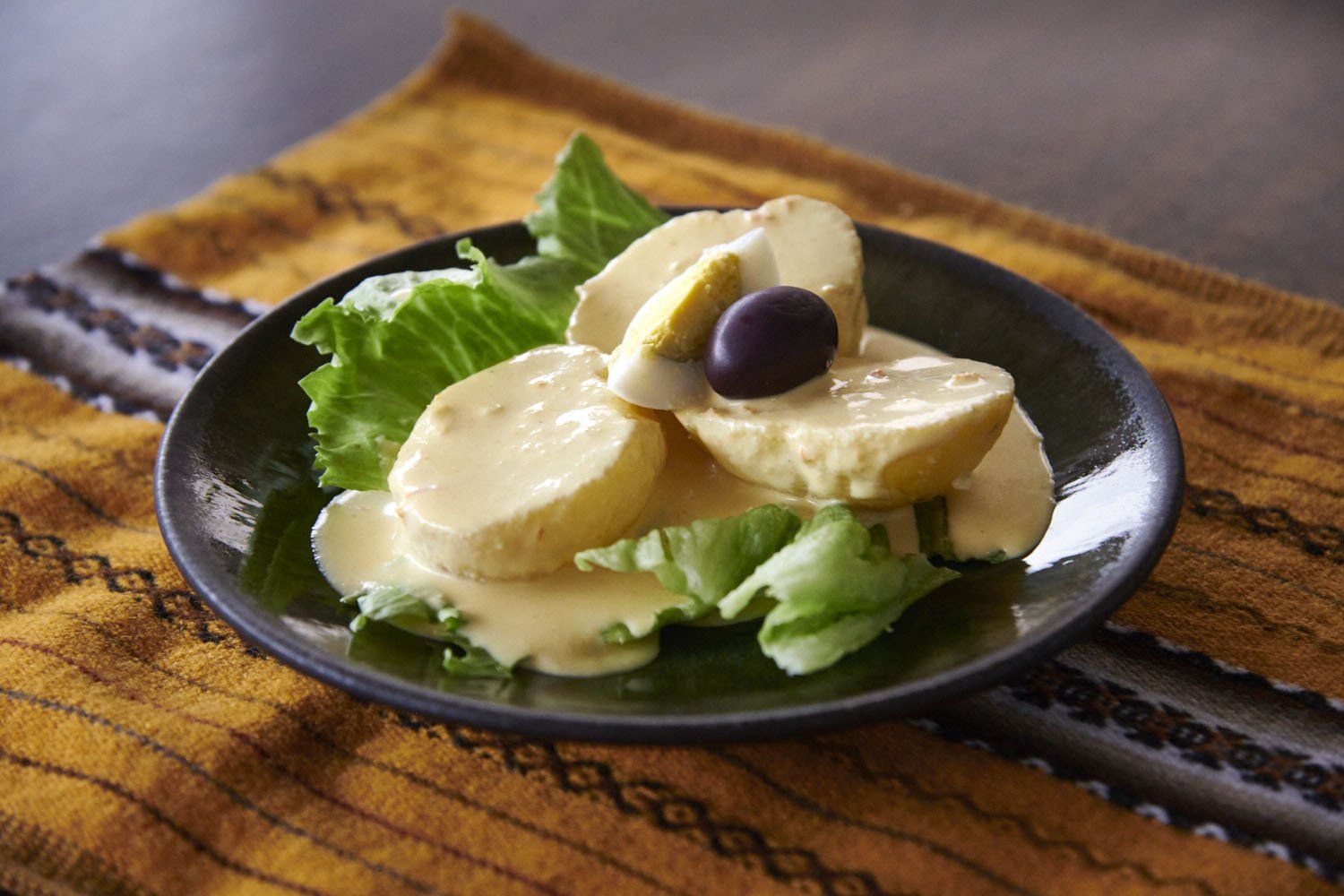Green salad with banana slices and a black olive on a black plate over a wooden table.