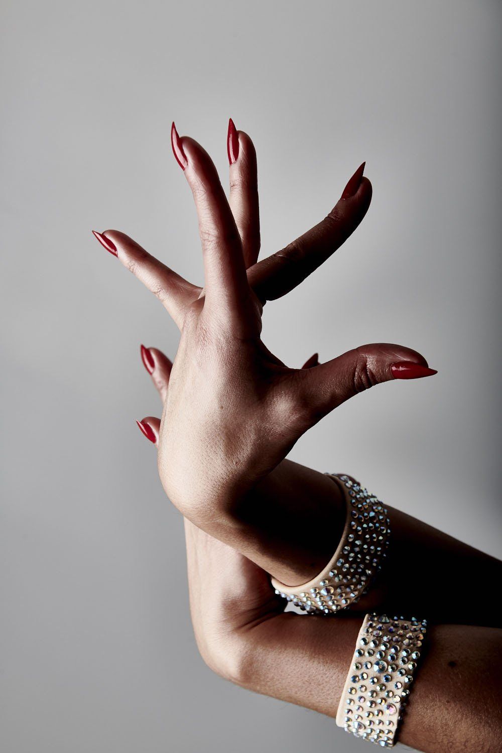 Hand with long red nails making a dance-like pose, wearing silver bracelets on a neutral background