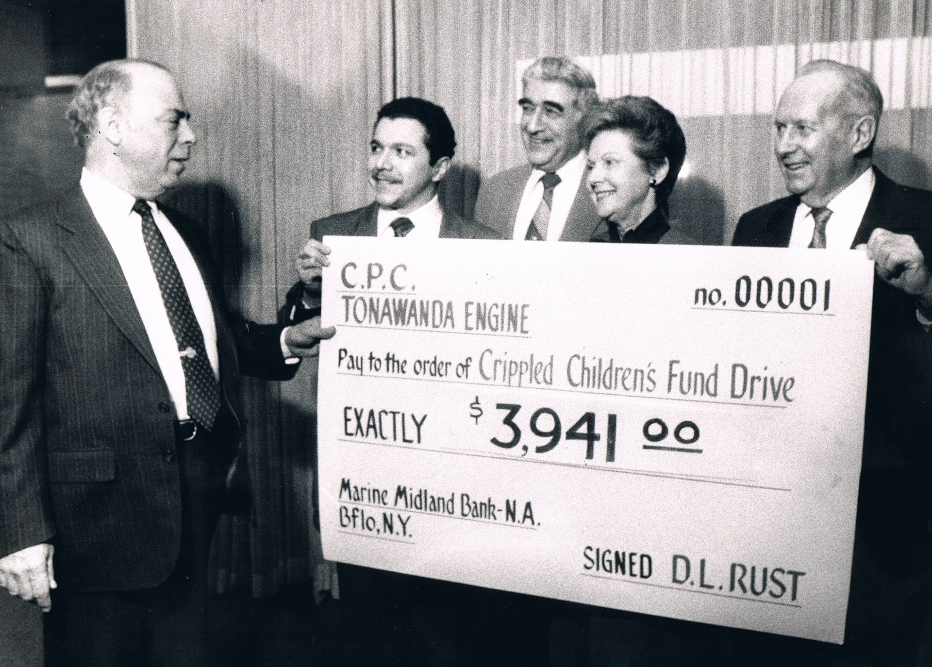 Men holding a giant check at a charity drive presentation, with “$3,941” and “Children’s Fund Drive” visible