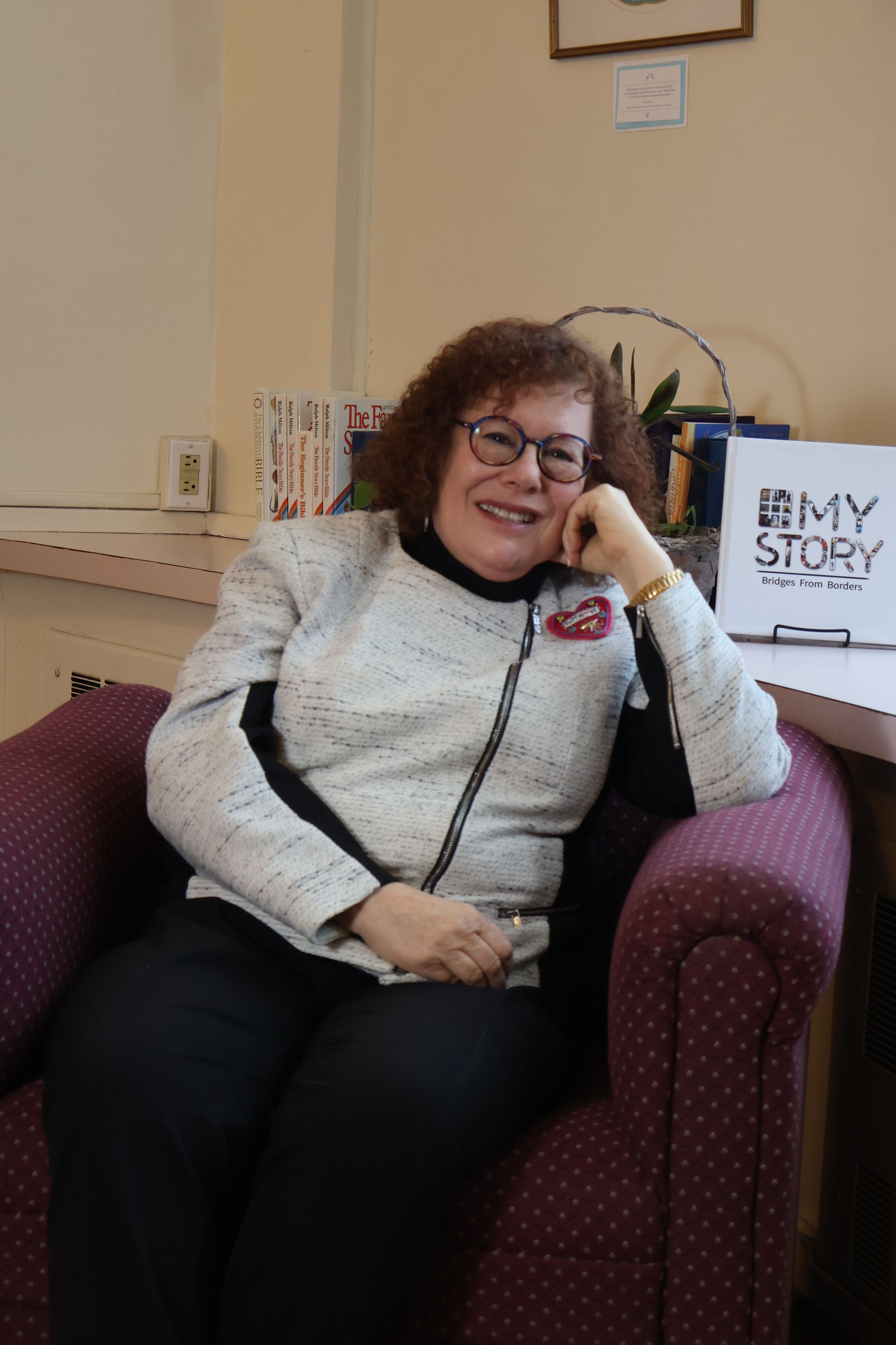 Smiling woman reclining in a purple armchair beside a sign that reads “STAY”
