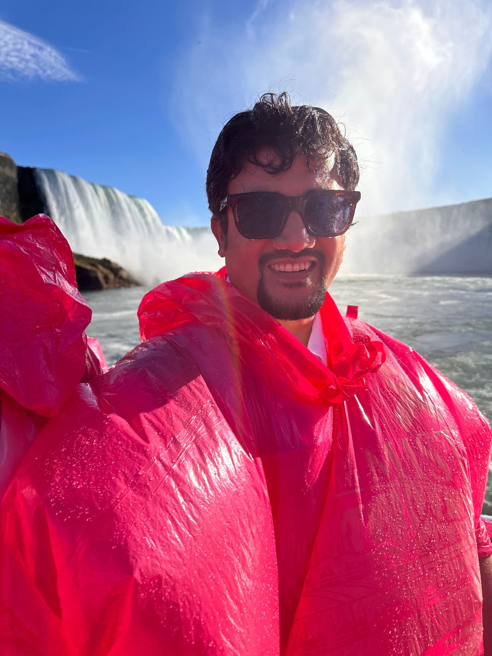 Person in a bright pink poncho smiling near a waterfall on a sunny day