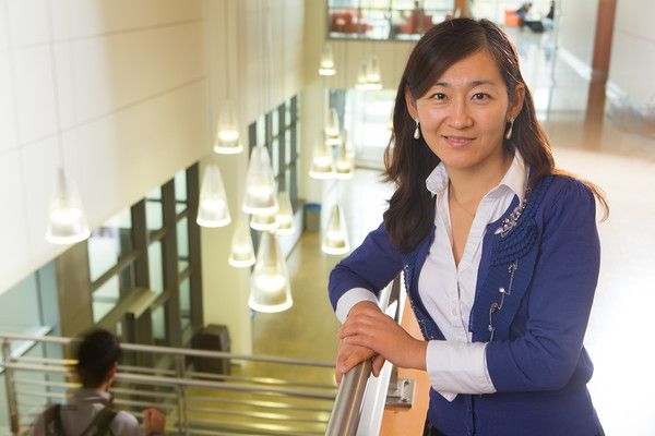 Woman in a blue blazer leaning on a railing in a bright indoor atrium.