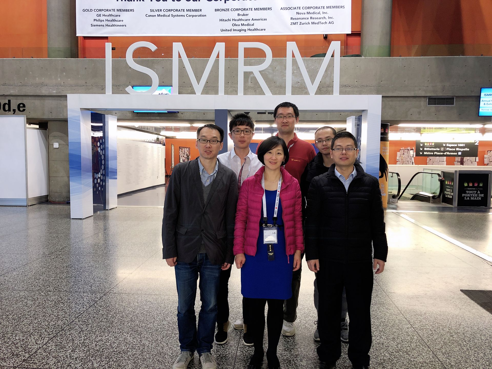 Four people posing in front of an ISMRM conference entrance, wearing lanyards