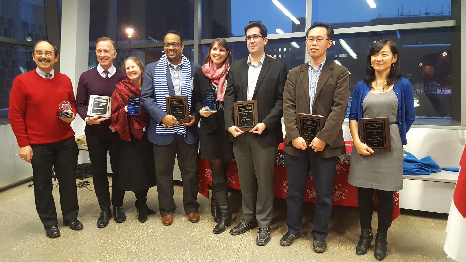 Group of people standing indoors at an award ceremony, several holding plaques and smiling.