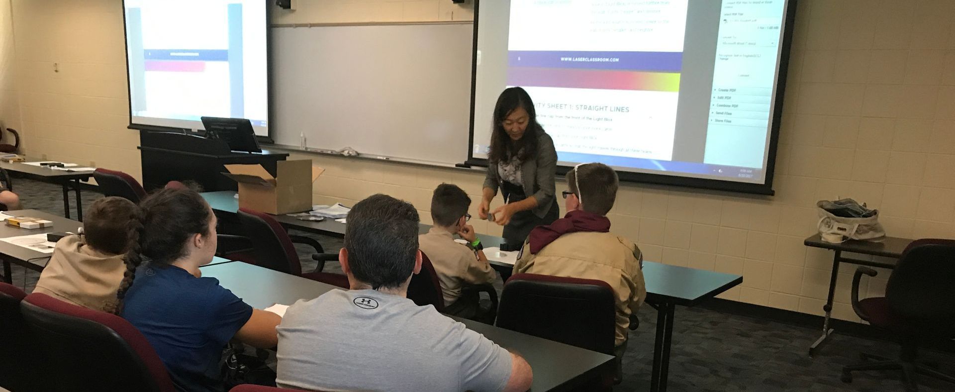 Classroom presentation with students seated and a speaker near a projected screen