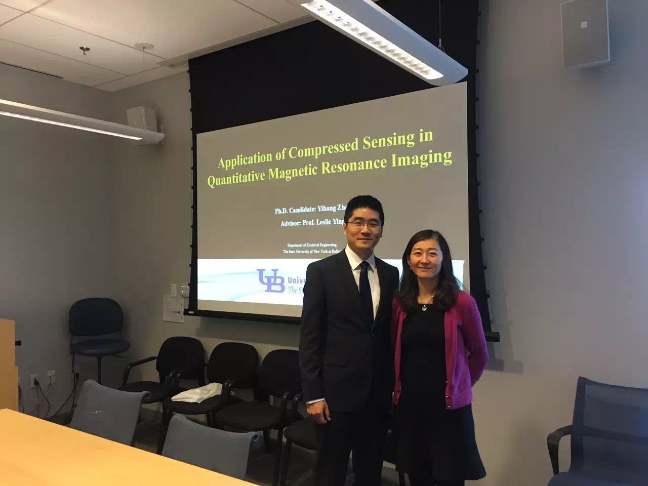 Two presenters standing in a classroom beside a projected slide on automated seeding in imaging