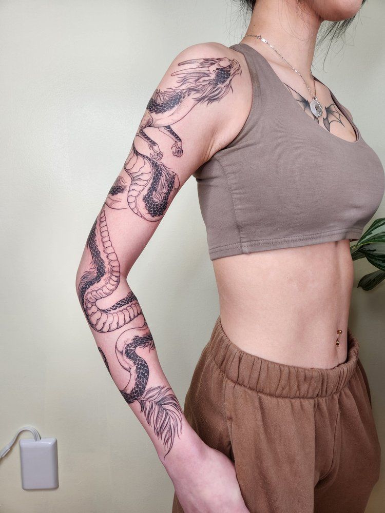 Side view of a person wearing a taupe crop top and brown pants, showing a full-arm tattoo.