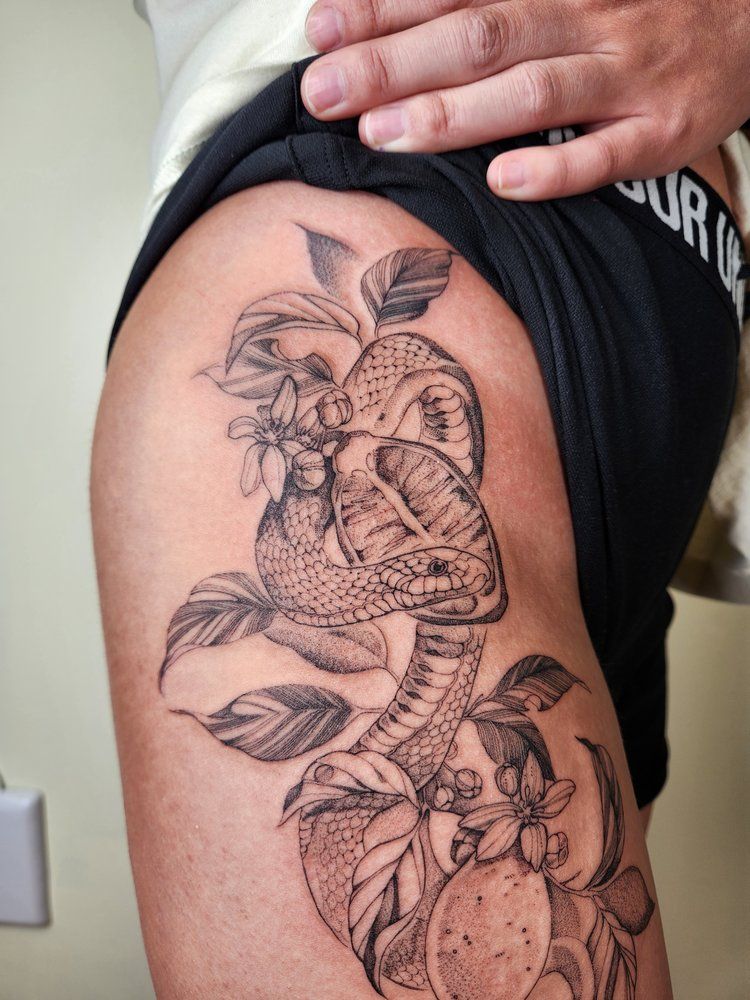 Arm tattoo of a floral butterfly and orange design on an upper arm, with a hand lifting the shirt sleeve.