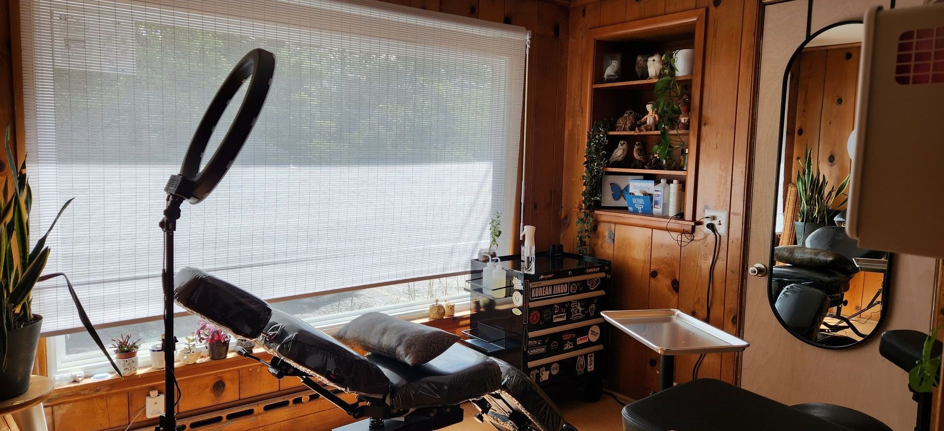Cozy wood-paneled room with a window, exercise bike, ring light, and shelves with plants and decor