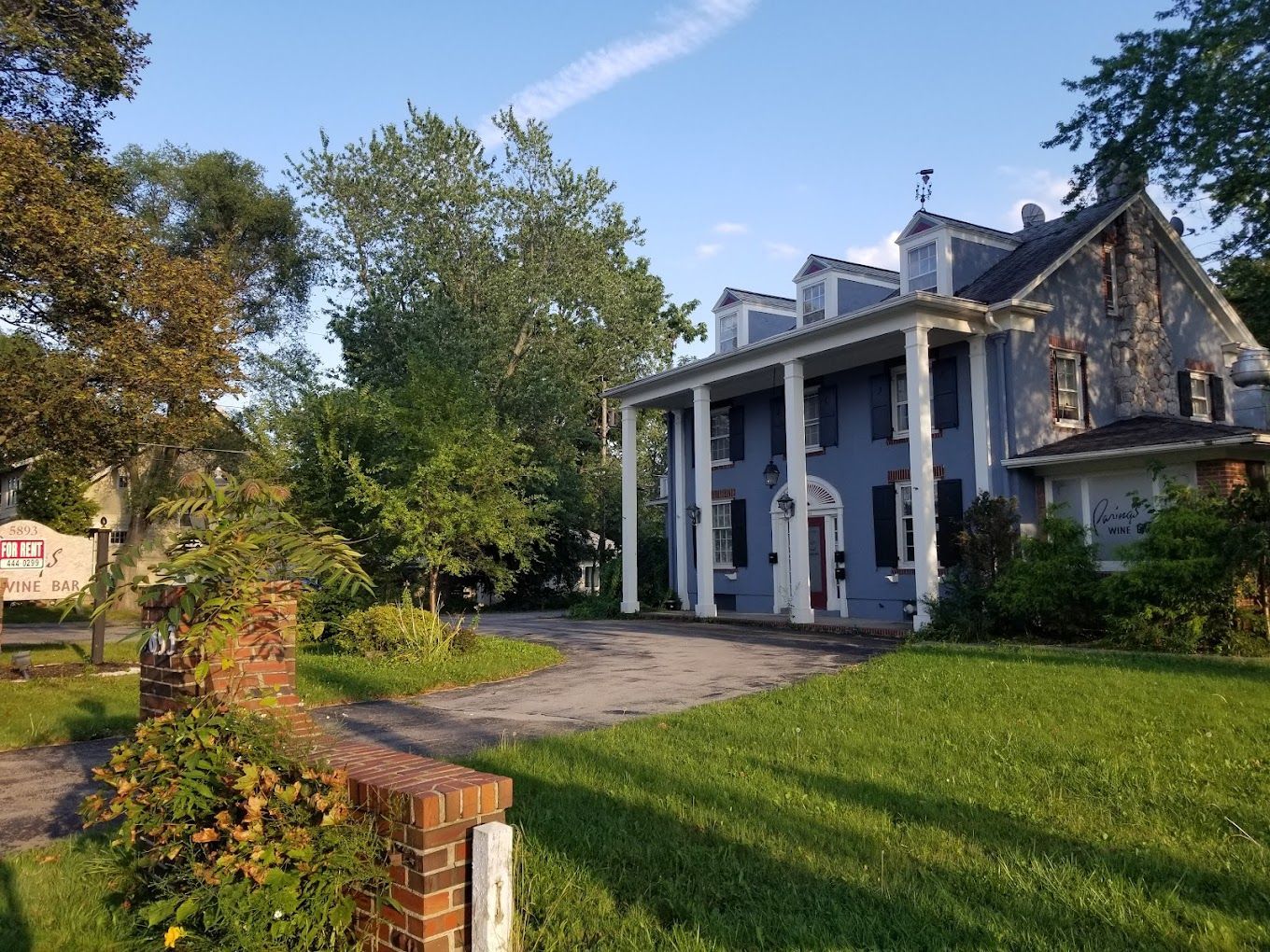 Large white house with tall columns beside a curved driveway and green lawn, viewed on a sunny day