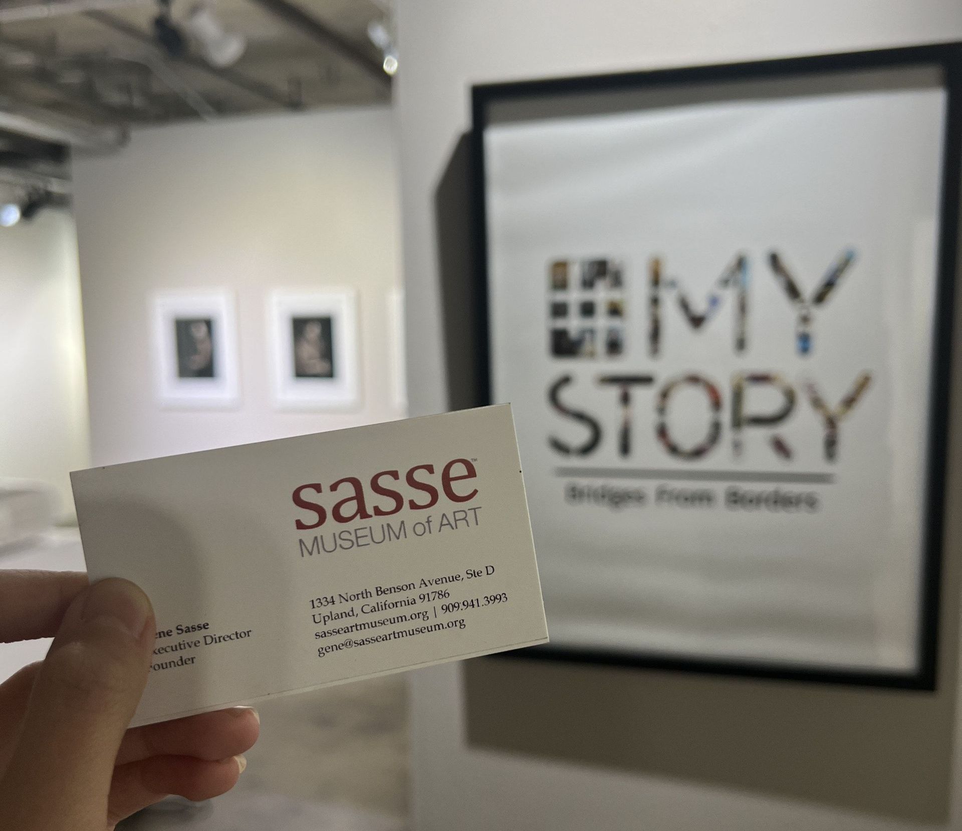 Hand holding a “sasse” card in front of an “MY STORY” sign in a gallery-like space