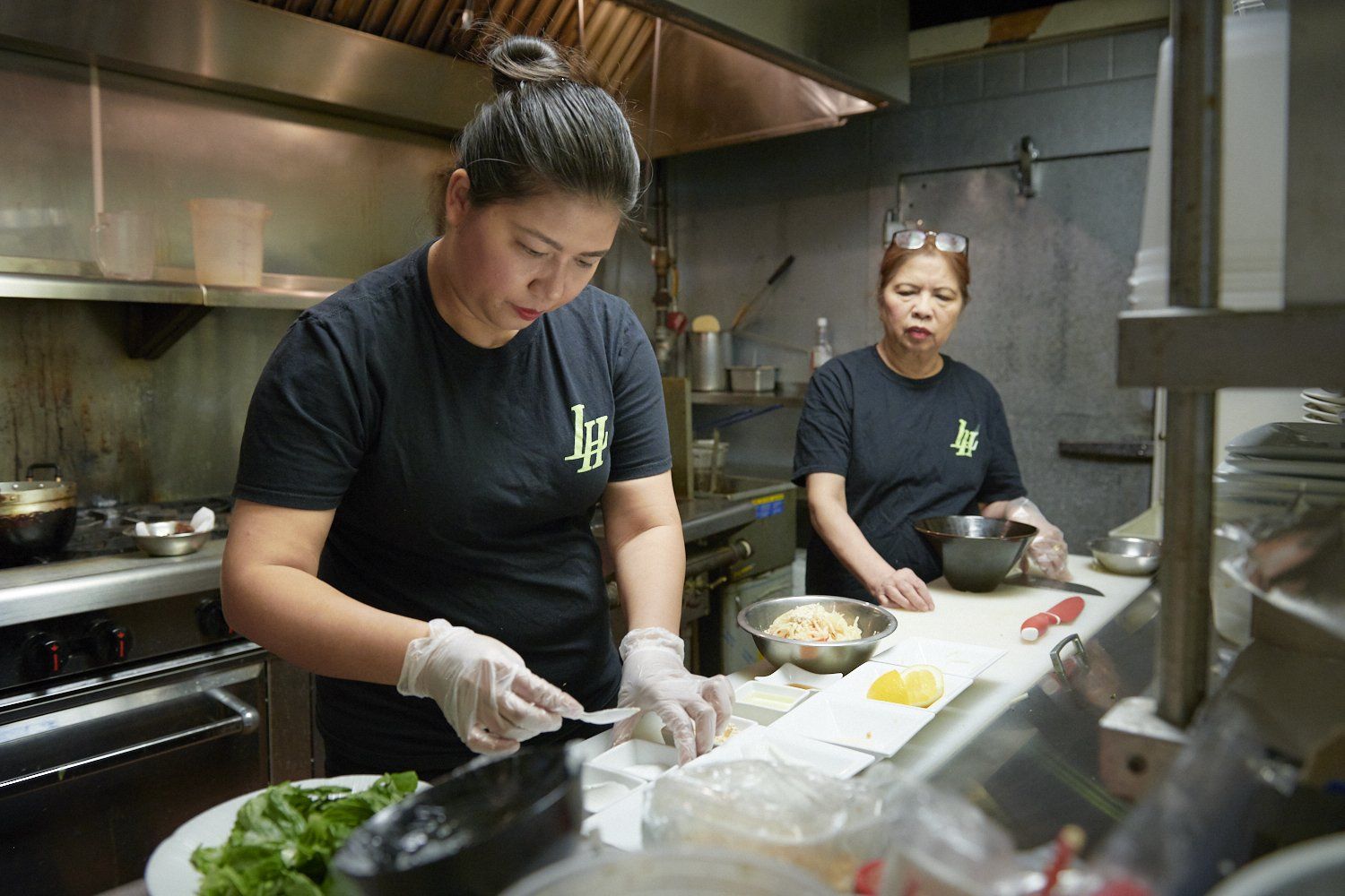 Two chefs in black shirts preparing food in a commercial kitchen
