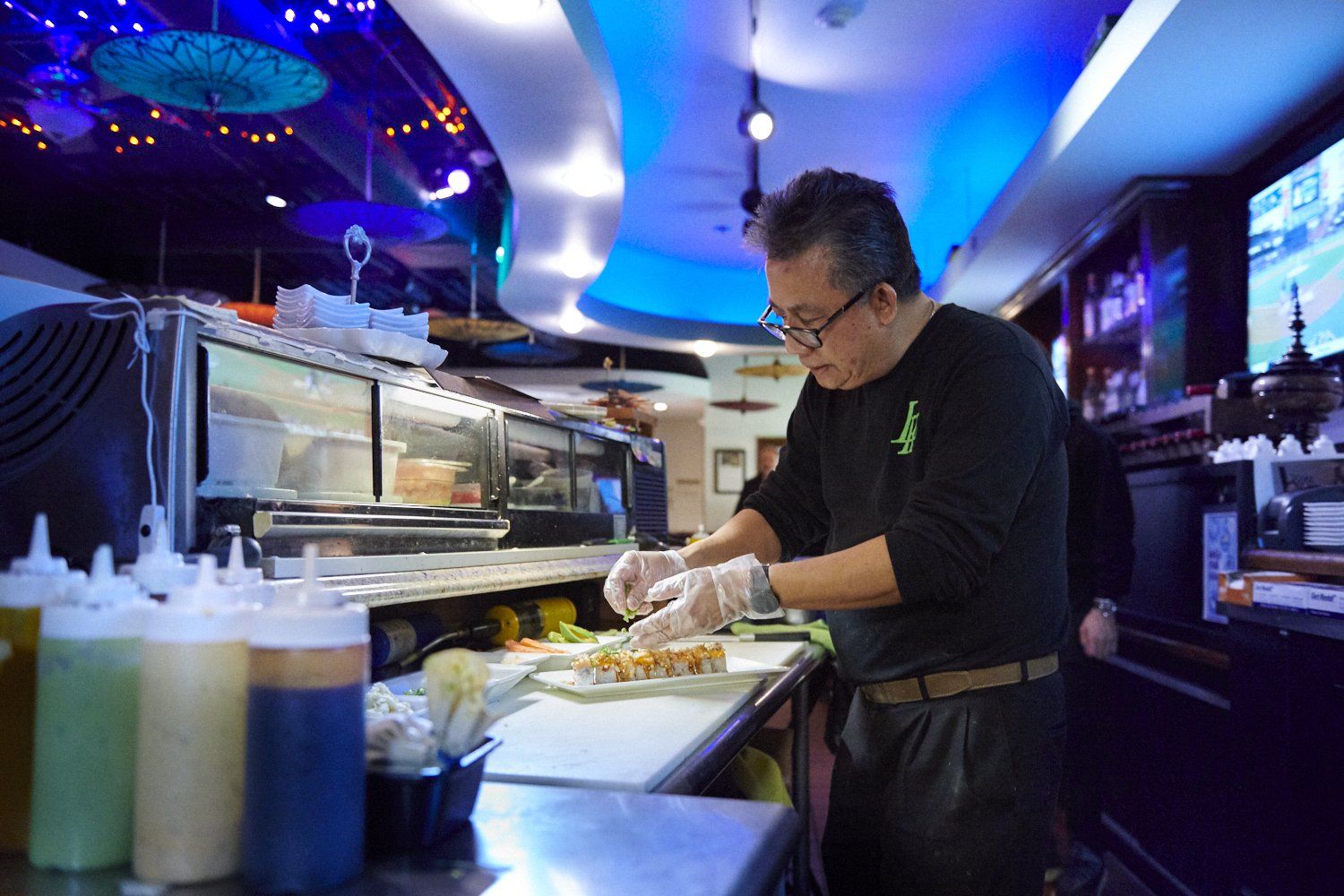 Chef preparing food at a restaurant counter under blue lighting