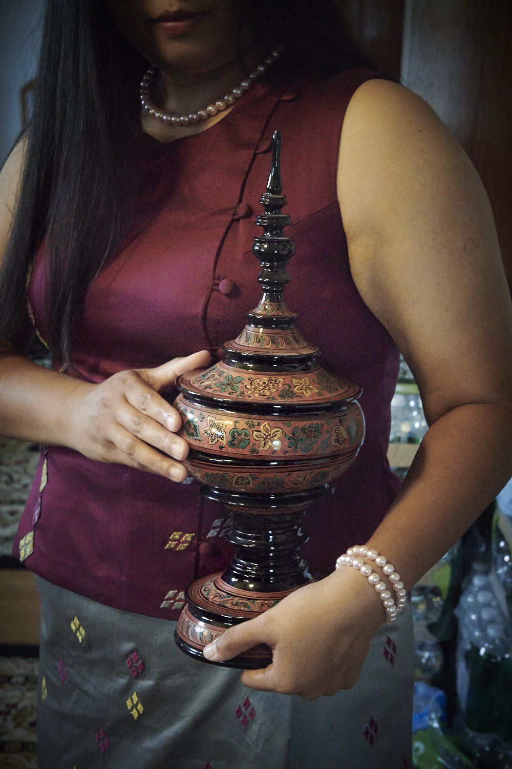 Woman holding a decorative bronze lantern against a dark background.