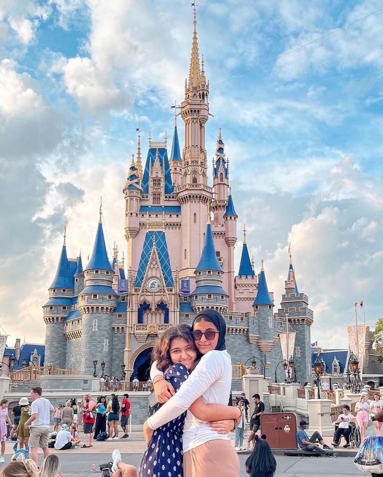 Two people hugging in front of Cinderella Castle at Disney World under a bright blue sky