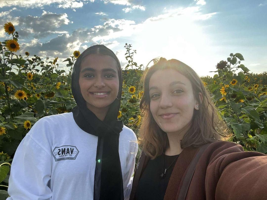 Two smiling people taking a selfie in a sunflower field at sunset
