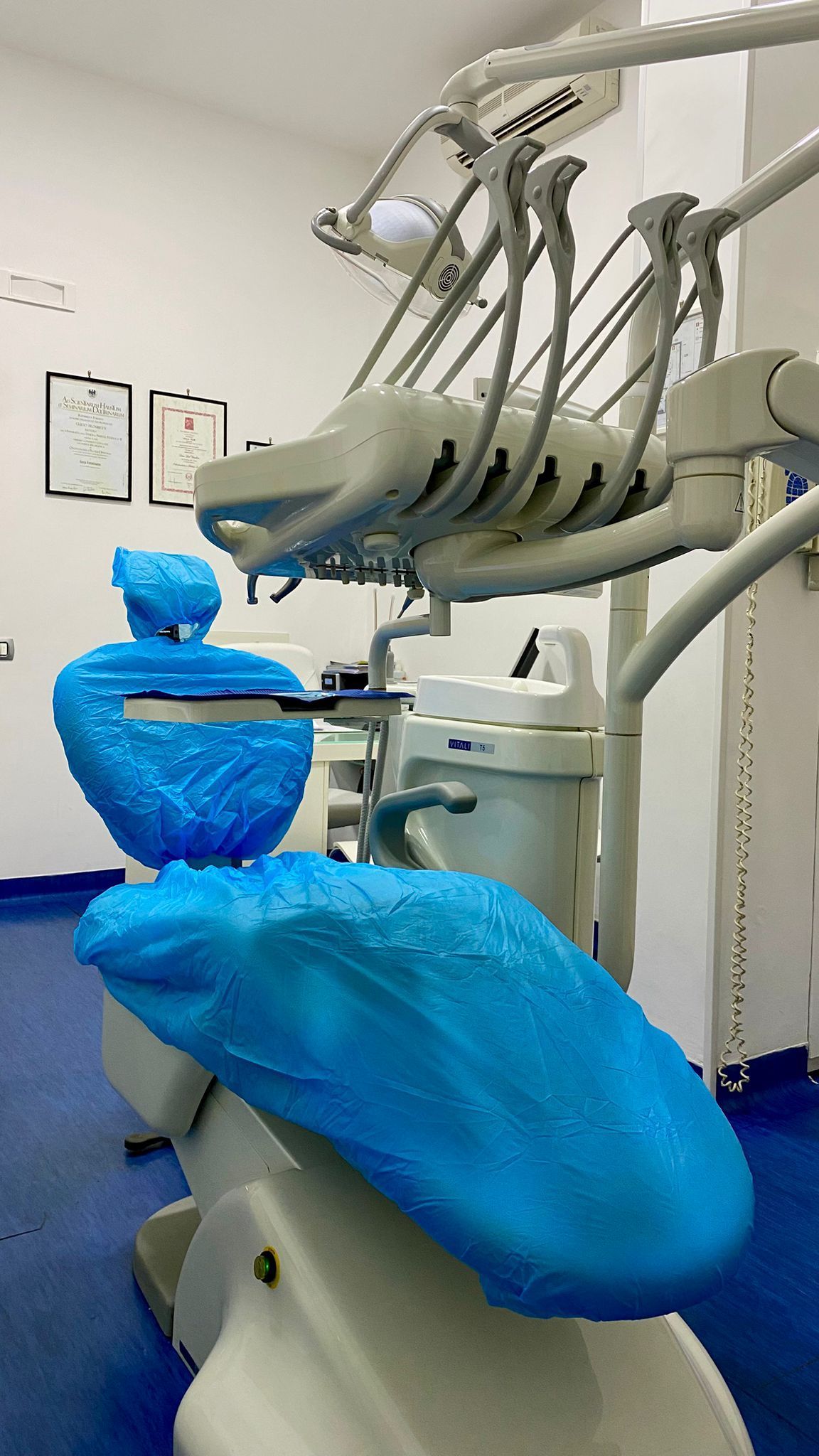 Poltrona odontoiatrica rivestita con rivestimenti protettivi blu in uno studio dentistico ben illuminato.