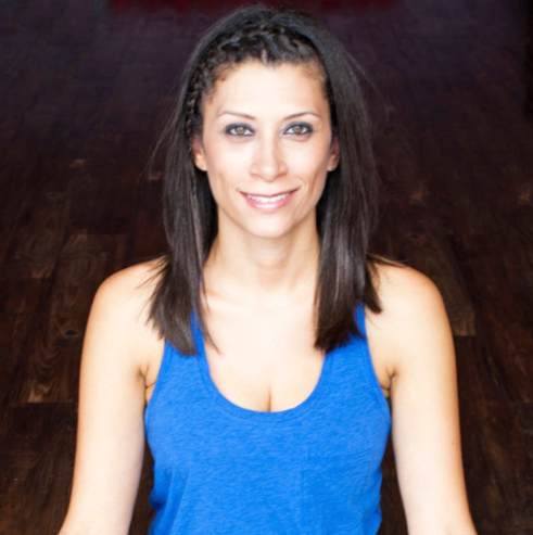 Alicia Smith, vinyasa yoga instructor at Uptown Yoga, smiling and sitting in a studio with wood floors.