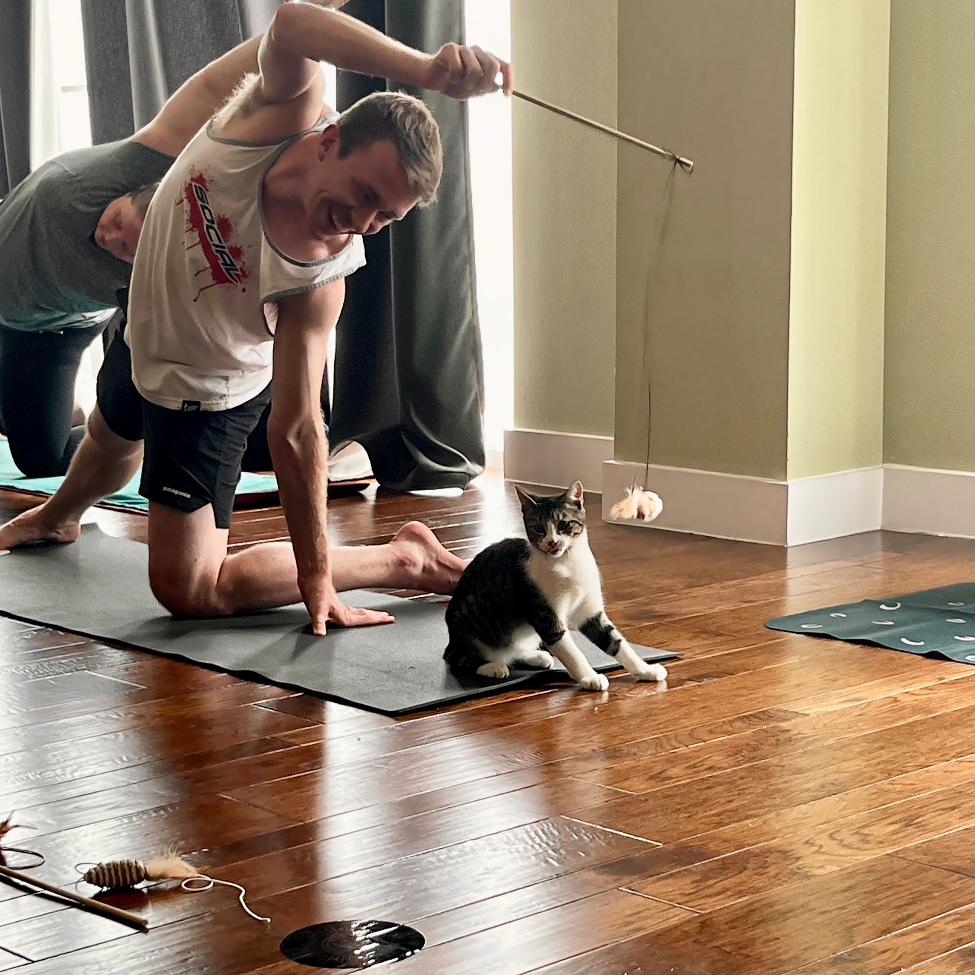 A student smiling and playing with a black and white rescue cat using a wand toy during a Kitty Yoga charity class at Uptown Yoga.