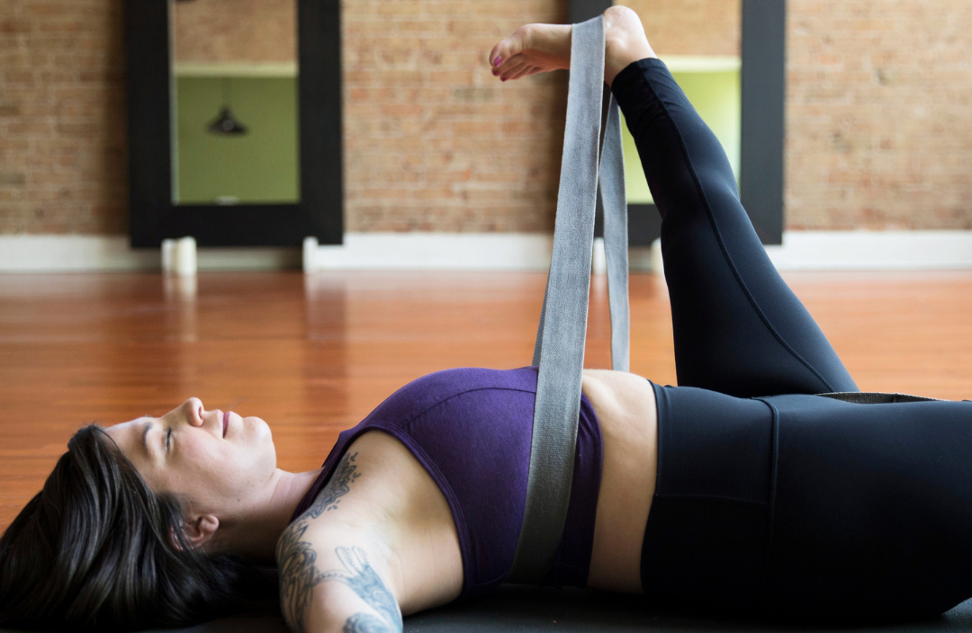 A student using a yoga strap for a reclining leg stretch during a relaxing Deep Stretch restorative class.