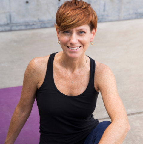 Headshot of Jenn Usherr-Davis, 500 E-RYT and lead trainer for the Uptown Yoga Teacher Training program, sitting on a purple yoga mat.